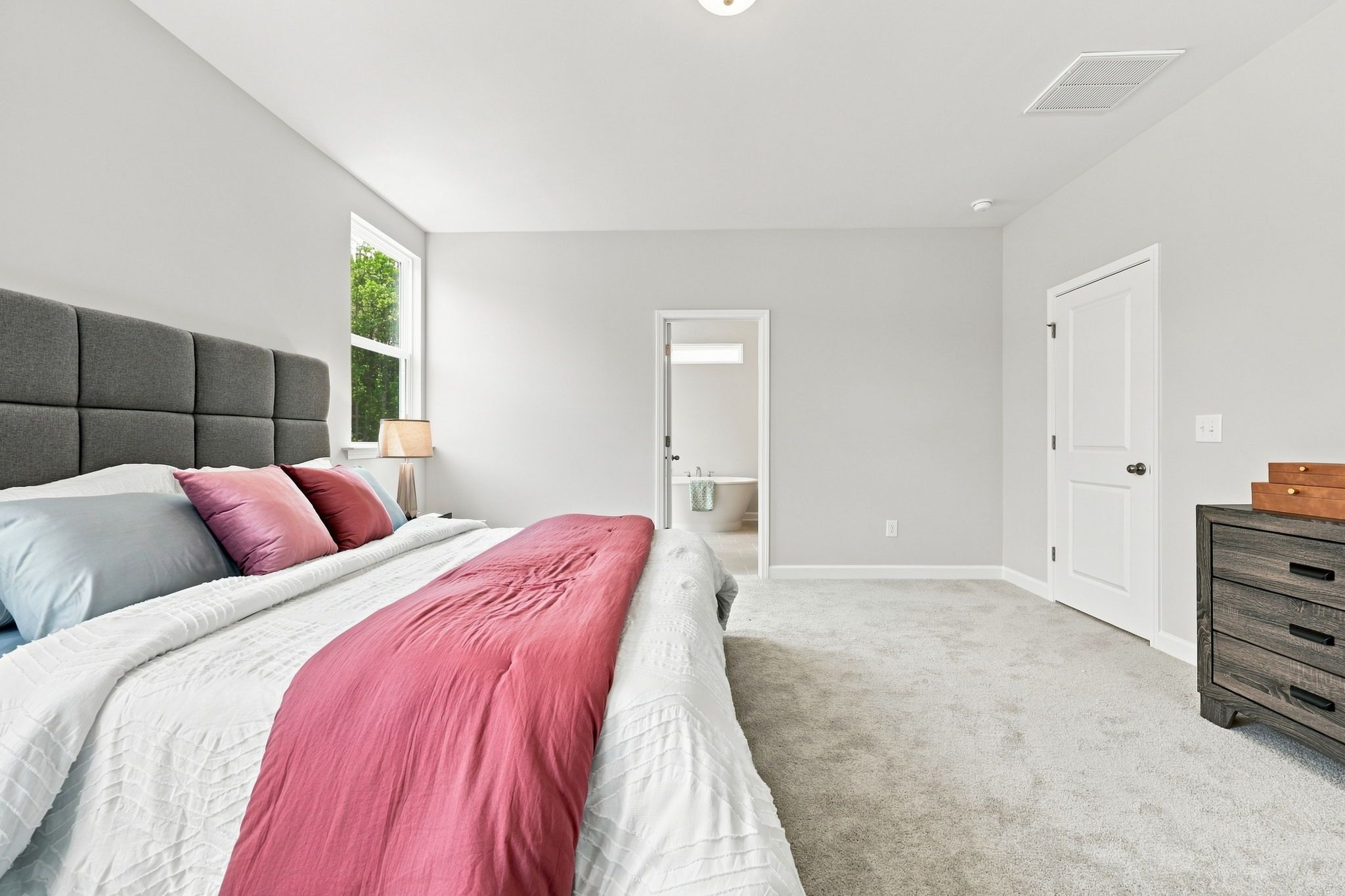 Spacious master suite in The Jordan A featuring plush carpeting, modern decor, and an attached primary bathroom.