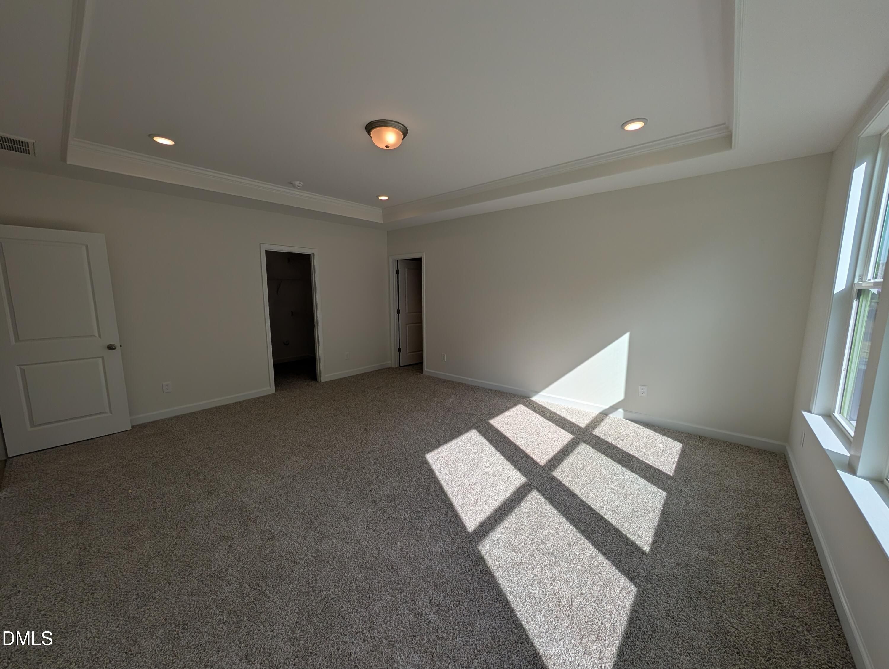 Bright primary bedroom with tray ceiling, carpet flooring, and large sunlit windows in Davidson Homes Magnolia A, Wendell Ridge