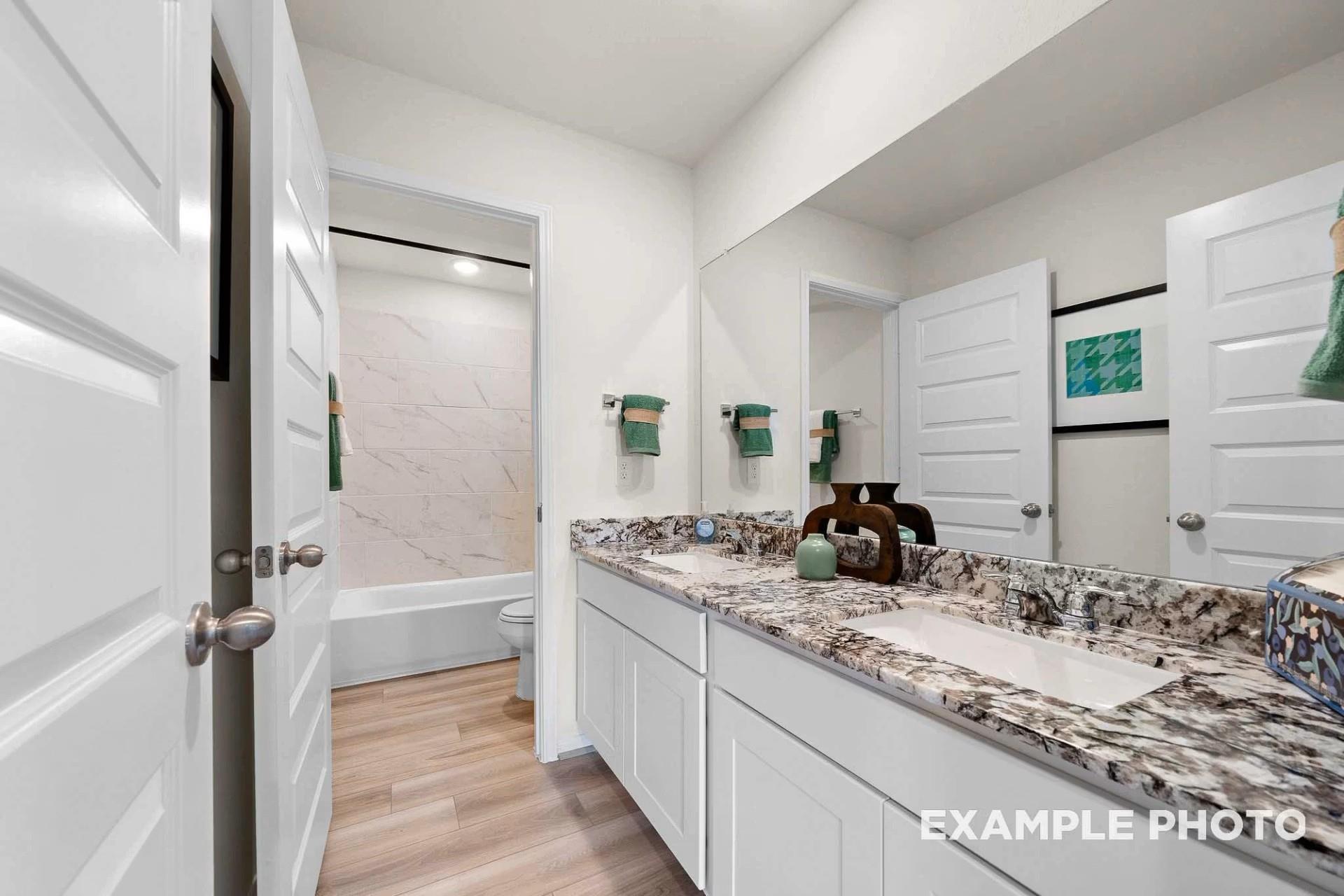 Modern double vanity bathroom with quartz countertops, white cabinets, and soaking tub in Davidson Homes The Tierra B, Beasley, Texas