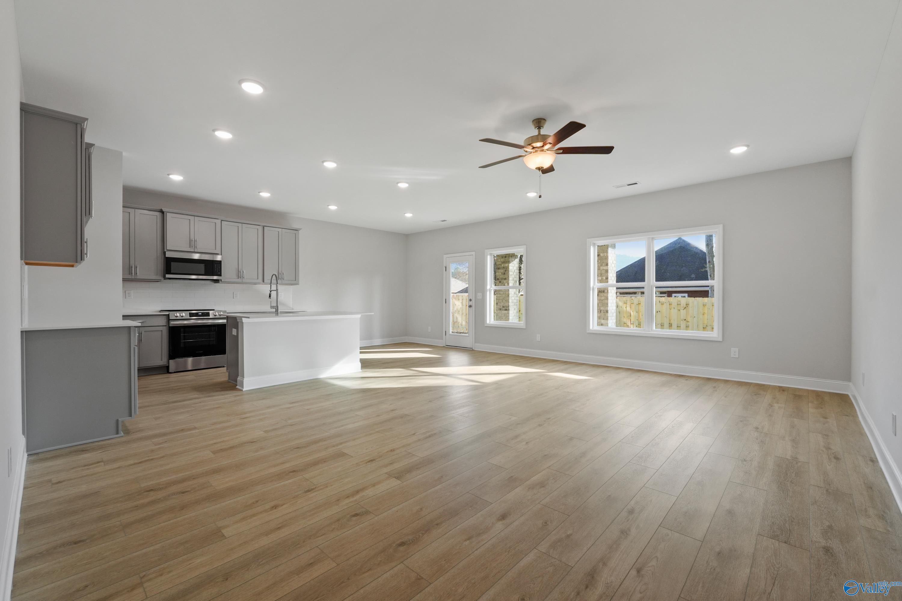 Open-concept kitchen with stainless appliances, gray cabinets, white island, hardwood floors, and large windows in The Camden B home, Huntsville, Alabama