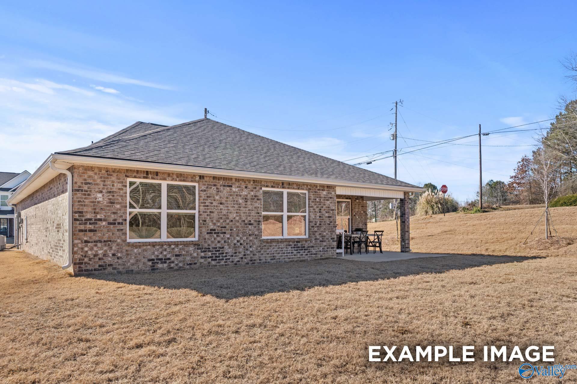 Covered side patio with seating beside single-story brick home, shingled roof, in Creek Grove, New Market, Alabama by Davidson Homes Franklin C