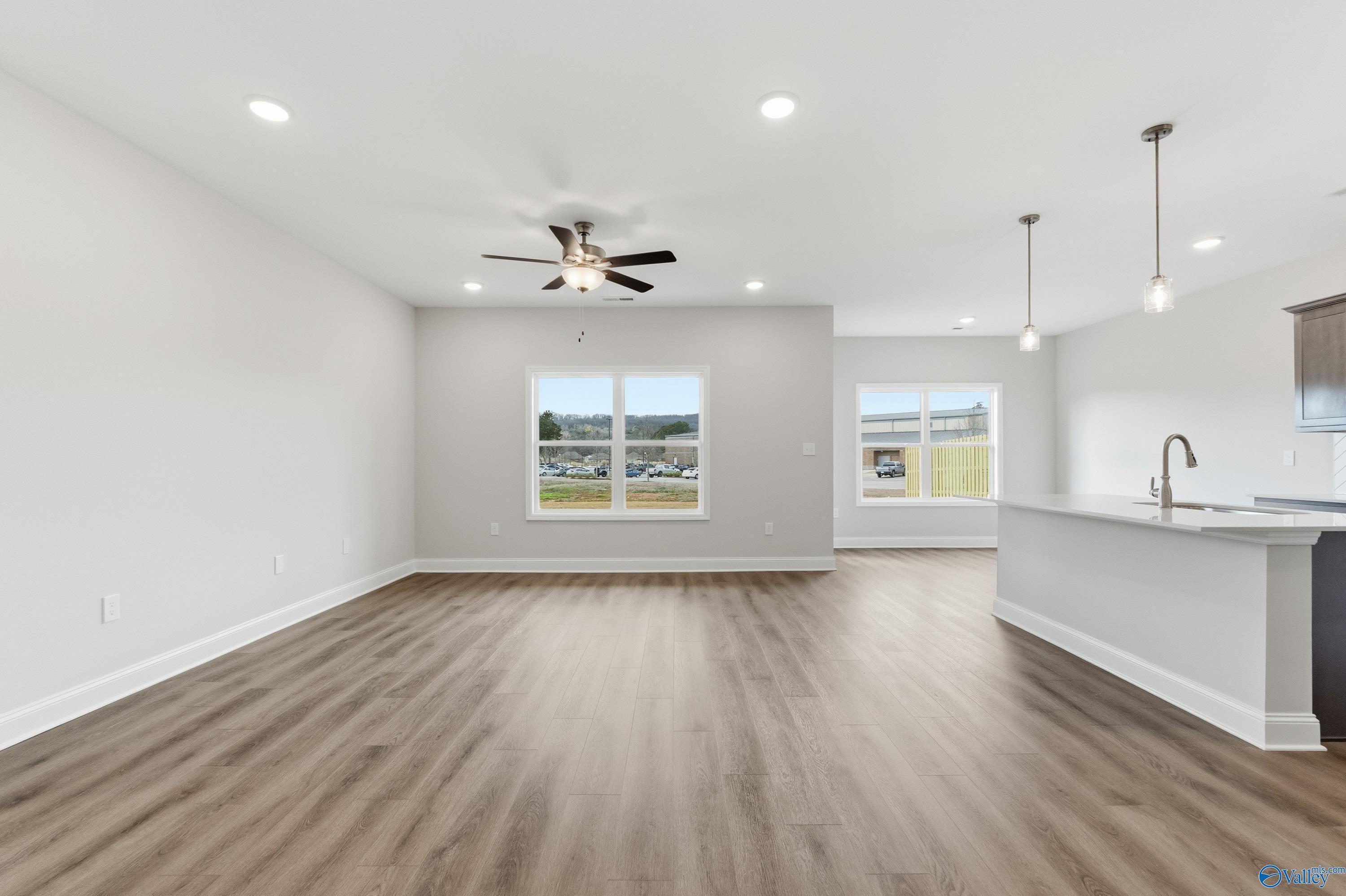 Spacious open great room with hardwood floors, ceiling fan, and large windows open to modern kitchen in The Asheville C, Huntsville AL