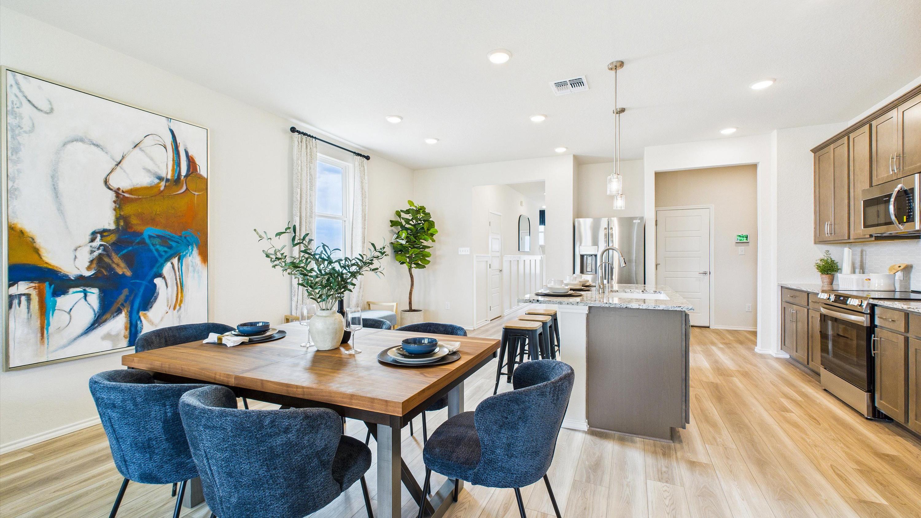 Open-concept dining area with wooden table, blue chairs, abstract art, and adjacent modern kitchen at Fairway Crossing in Converse Texas