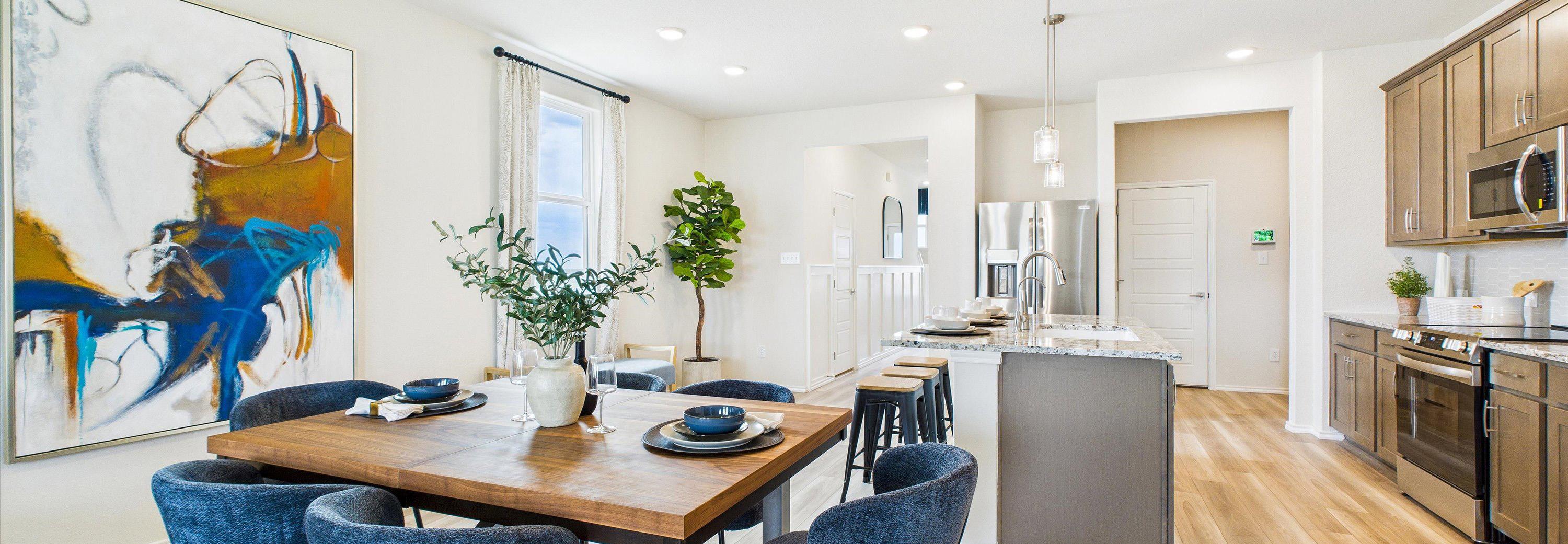 Open-concept dining area with wooden table, blue chairs, abstract art, and adjacent modern kitchen at Fairway Crossing in Converse Texas