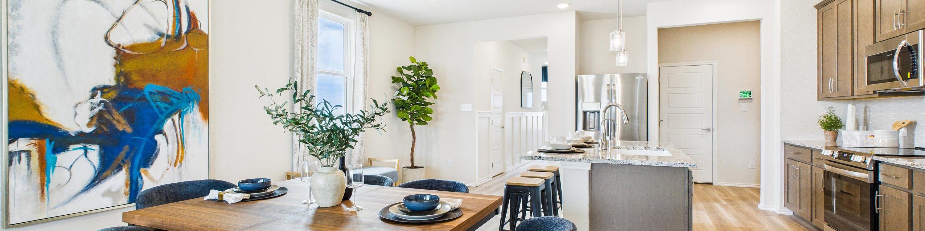 Open-concept dining area with wooden table, blue chairs, abstract art, and adjacent modern kitchen at Fairway Crossing in Converse Texas