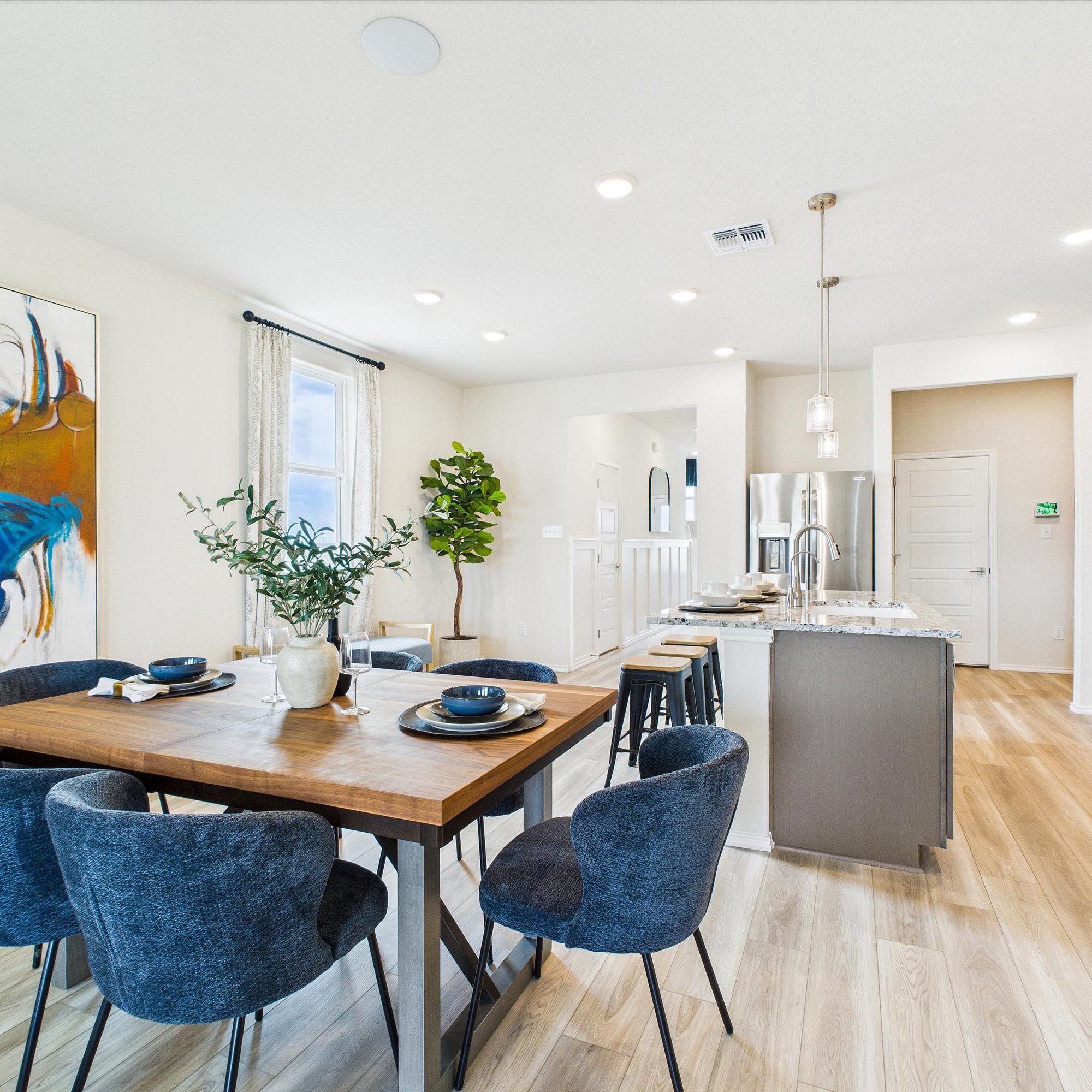 Open-concept dining area with wooden table, blue chairs, abstract art, and adjacent modern kitchen at Fairway Crossing in Converse Texas