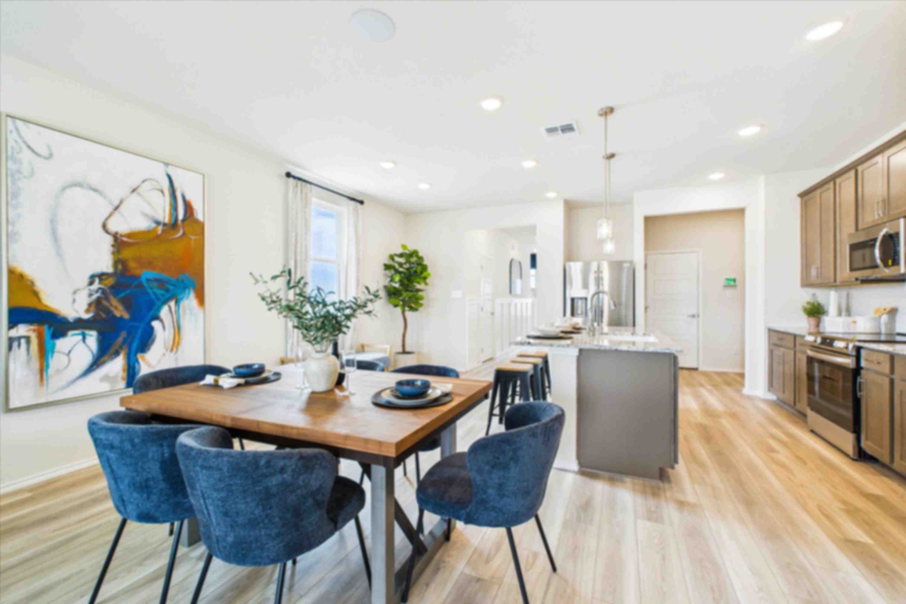 Open-concept dining area with wooden table, blue chairs, abstract art, and adjacent modern kitchen at Fairway Crossing in Converse Texas