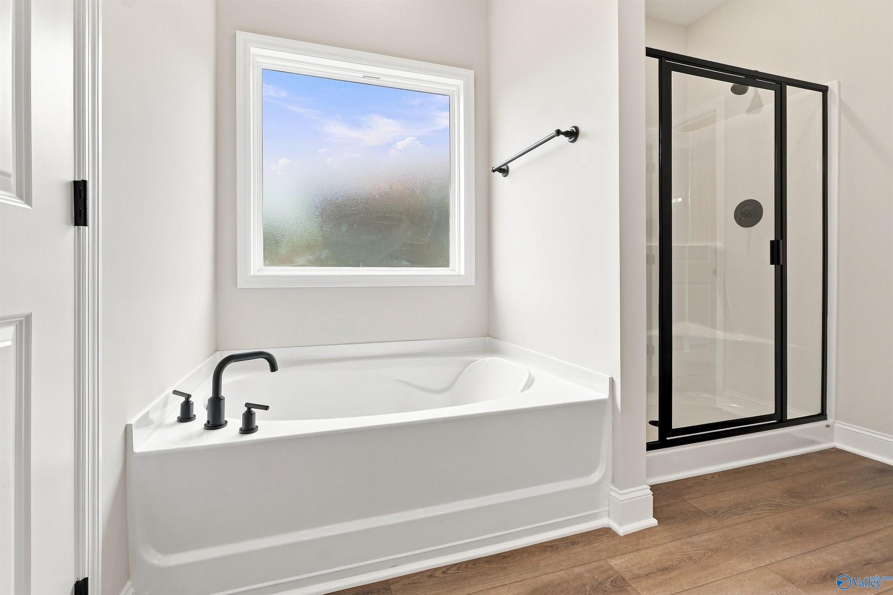 Soaking tub with matte black fixtures beside glass walk-in shower in master bath of Davidson Homes Everett B, Toney, Alabama