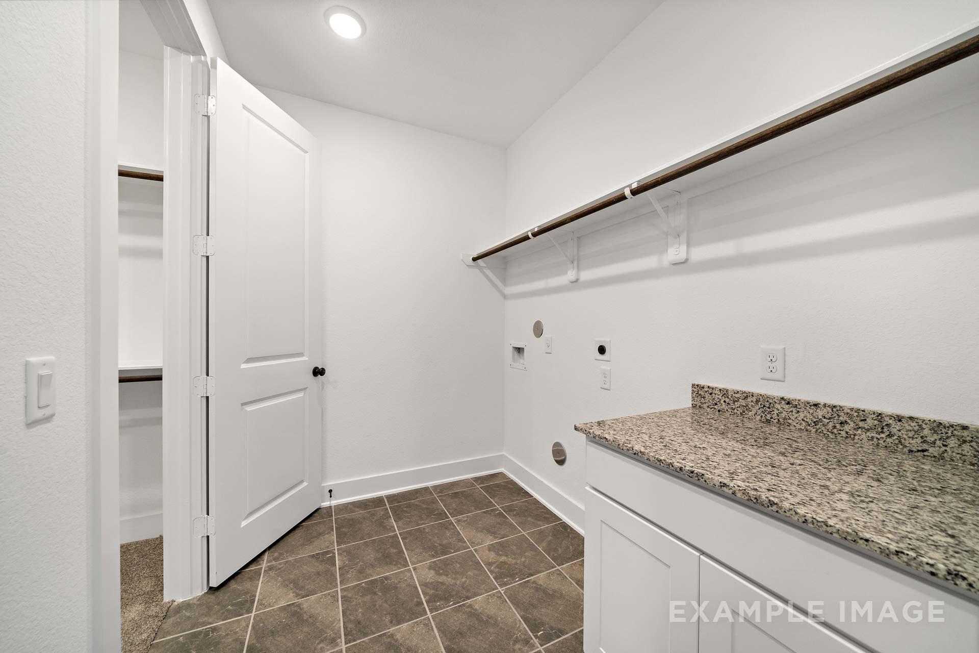 Spacious laundry room in The Victoria A with white cabinets, granite countertop, utility sink and built-in shelves
