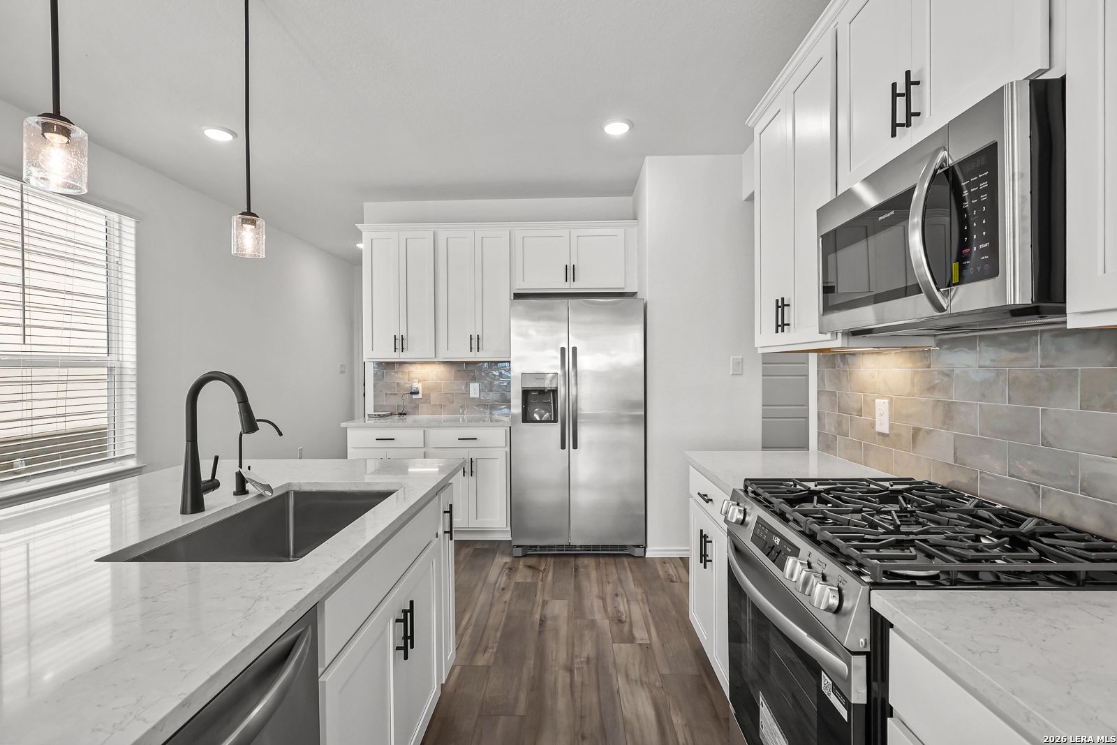 Modern kitchen with white cabinets, stainless steel appliances, and quartz island in The Gillian C home, San Antonio, TX.