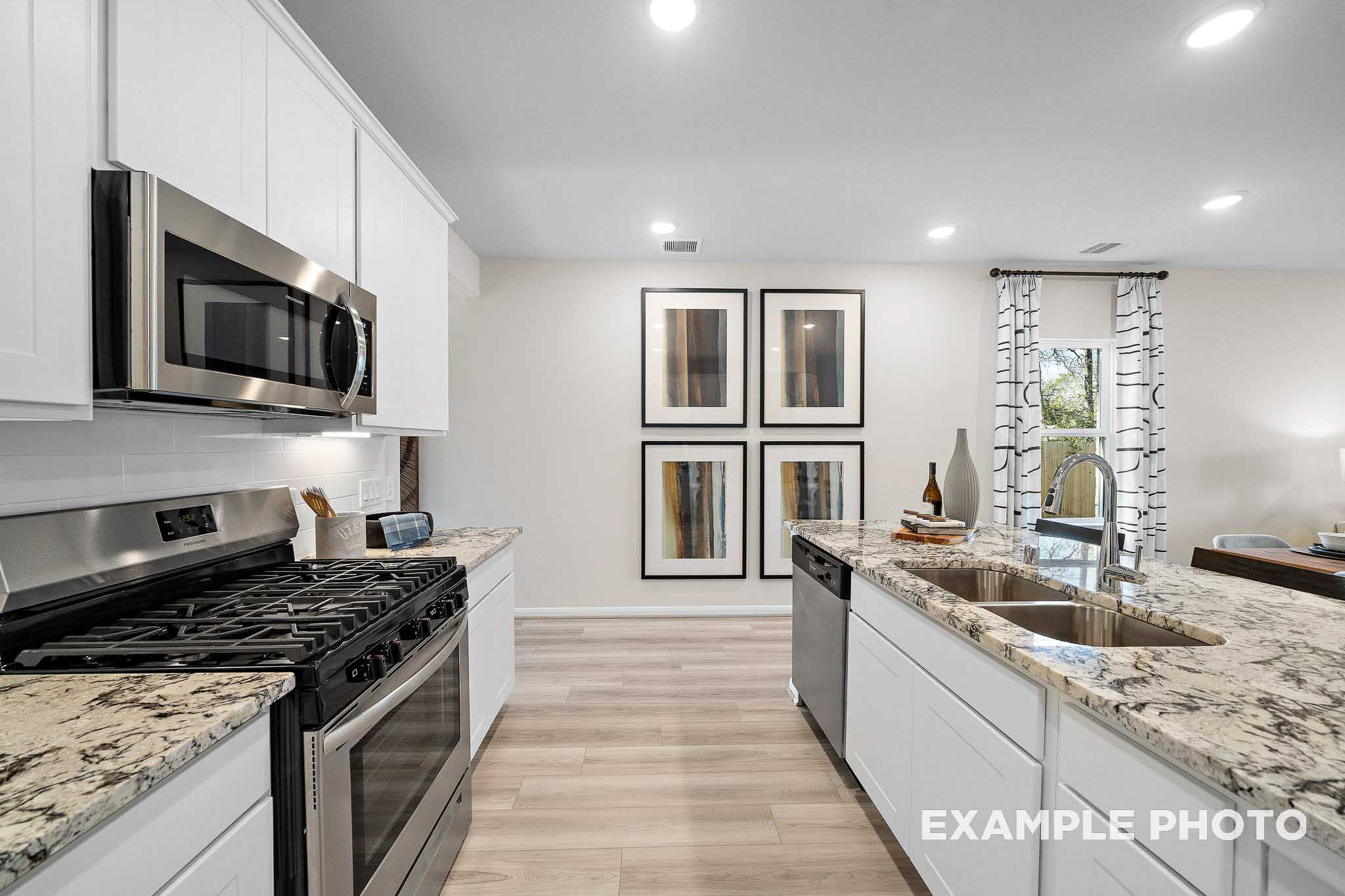 Spacious modern kitchen in The San Marcos B featuring white cabinets, granite island, stainless steel appliances, and hardwood floors