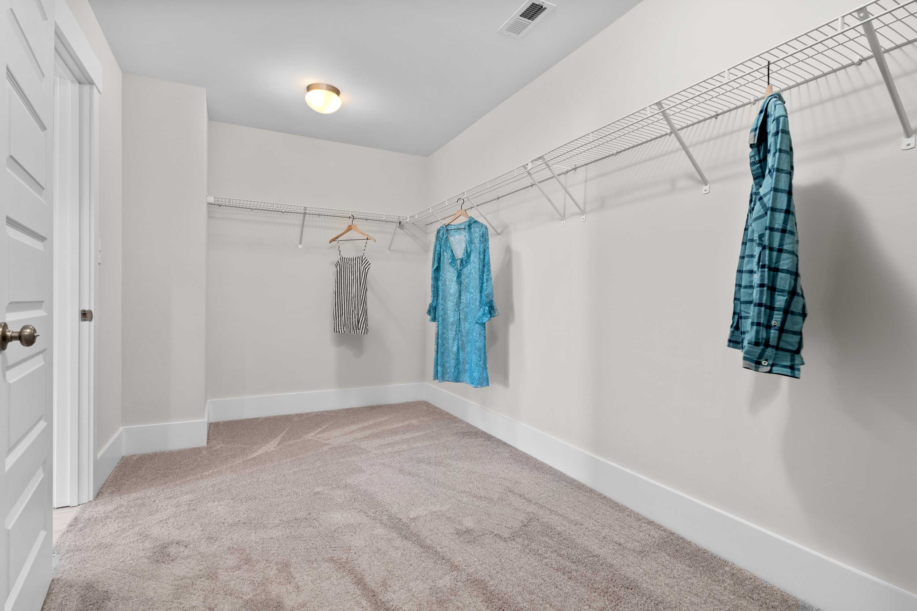 Spacious walk-in closet in The Chelsea A master suite, featuring wire shelving, hanging rods, and organized apparel on beige walls