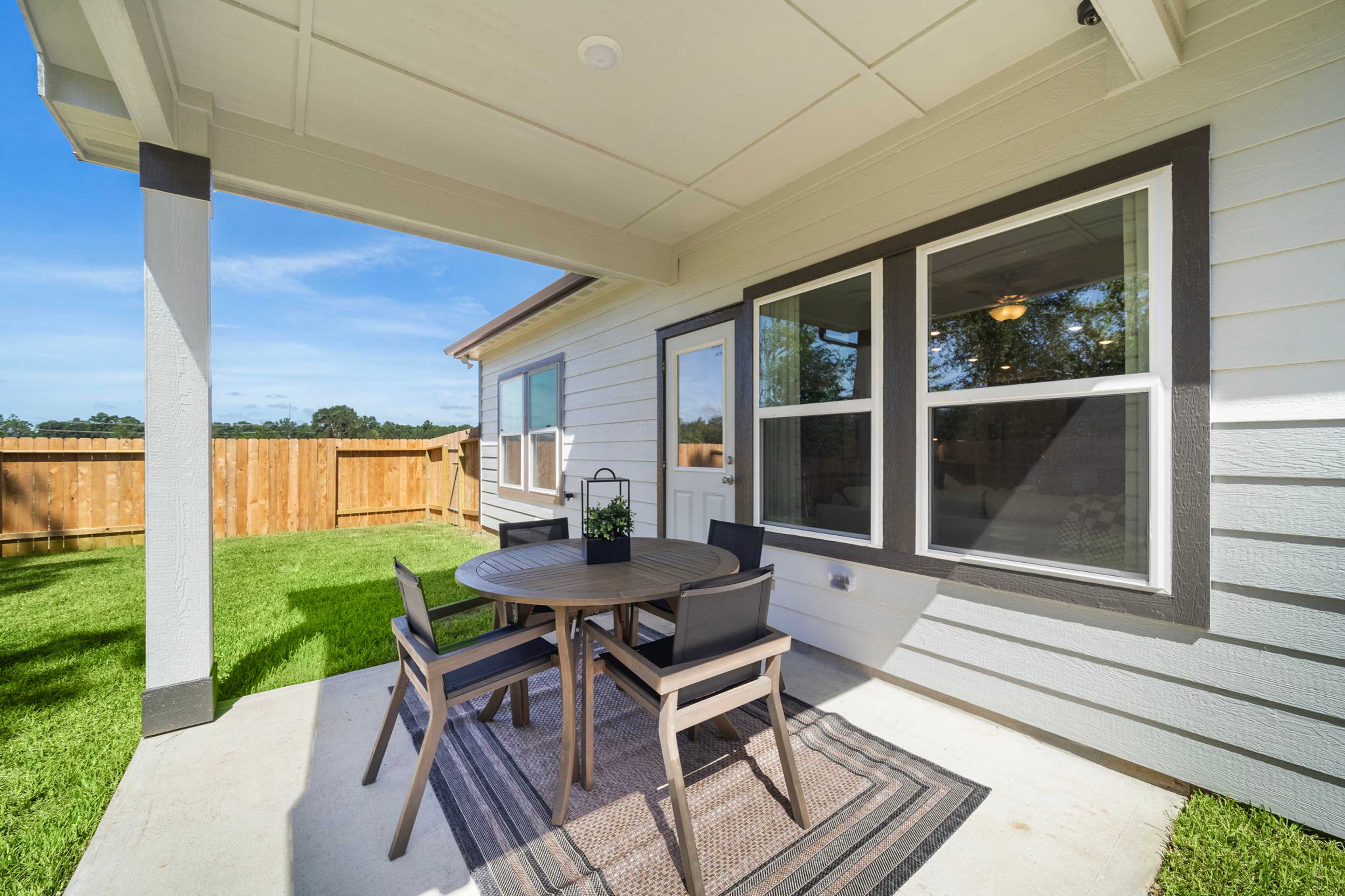 Covered patio with round wooden table and cushioned chairs at Caney Creek Place in Conroe Texas overlooking green lawn and home windows
