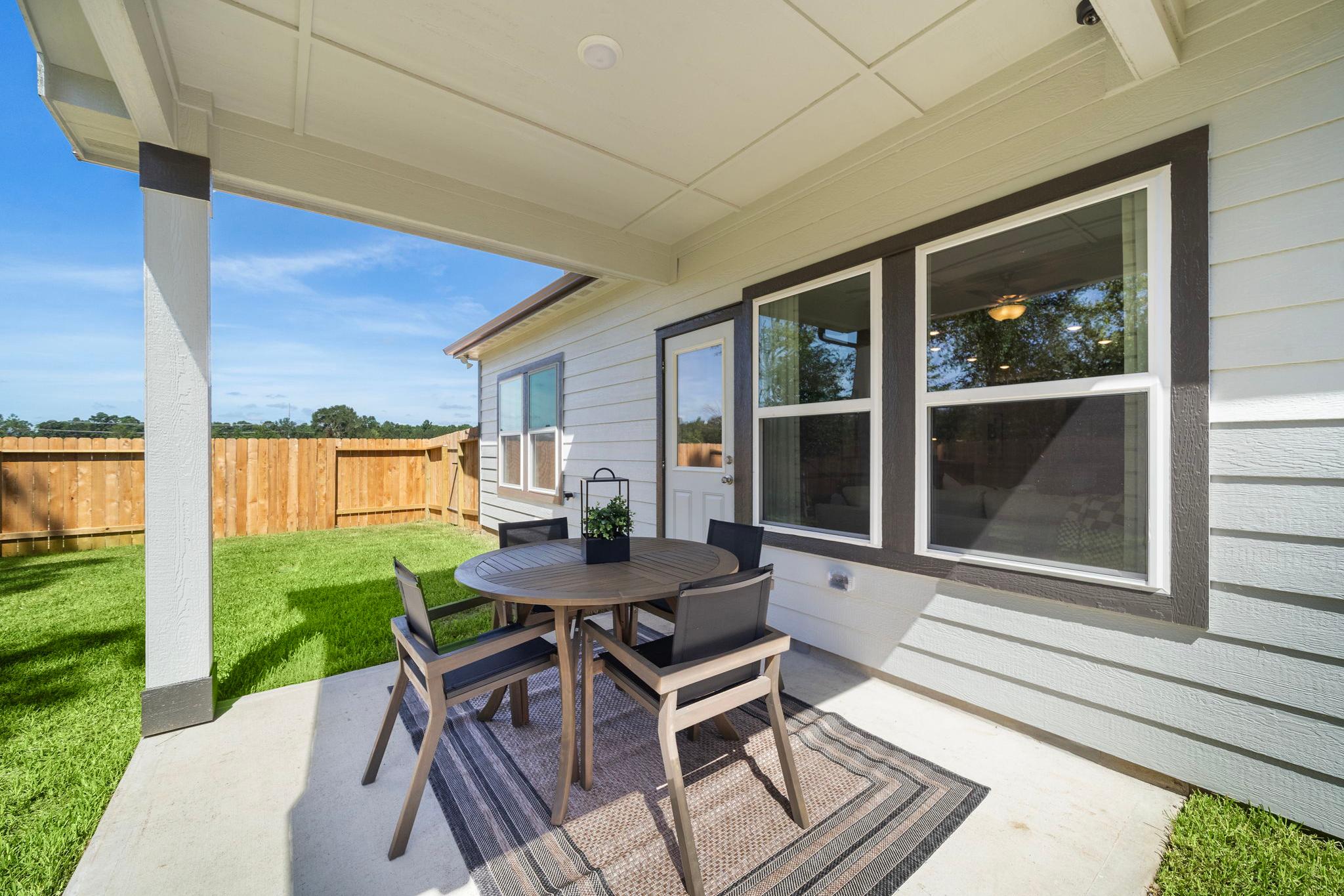 Covered patio with round wooden table and cushioned chairs at Caney Creek Place in Conroe Texas overlooking green lawn and home windows