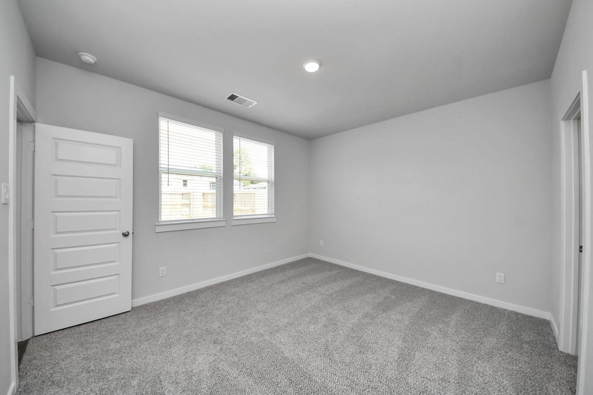 Bright bedroom with carpet flooring, dual windows, and white door in Davidson Homes The Frio F, Robins Landing, Houston