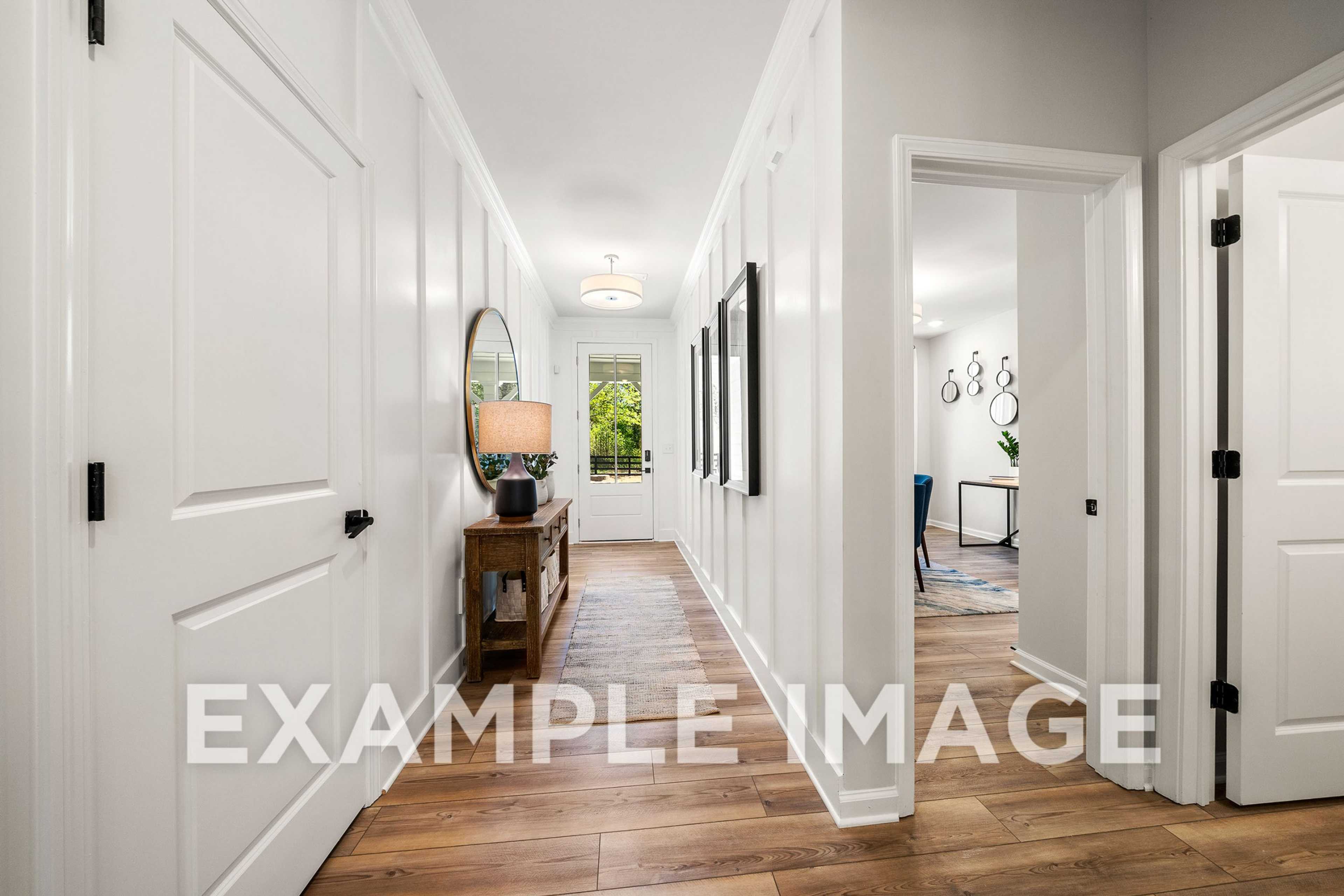 Spacious hallway in The Hickory A home design featuring white paneled walls, hardwood floors, arched doorways, and elegant console table