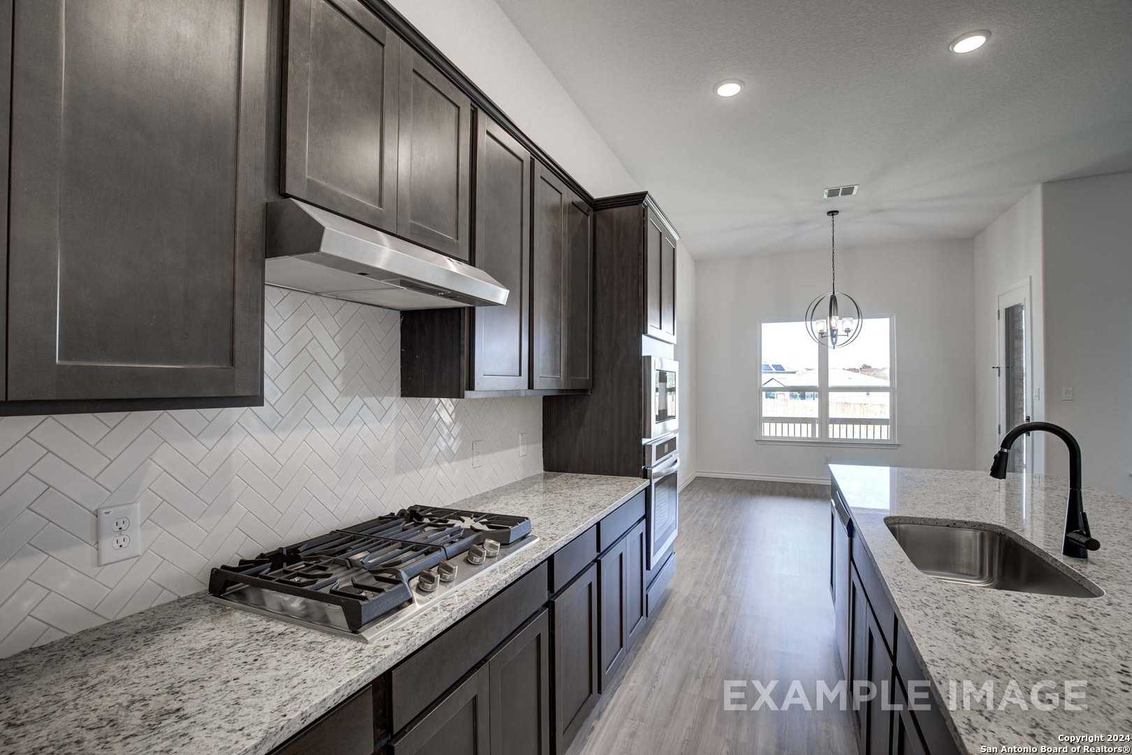 Modern kitchen featuring dark shaker cabinets, herringbone tile backsplash, granite counters, gas range, and stainless appliances in Davidson Homes The Garner C, Castroville, Texas