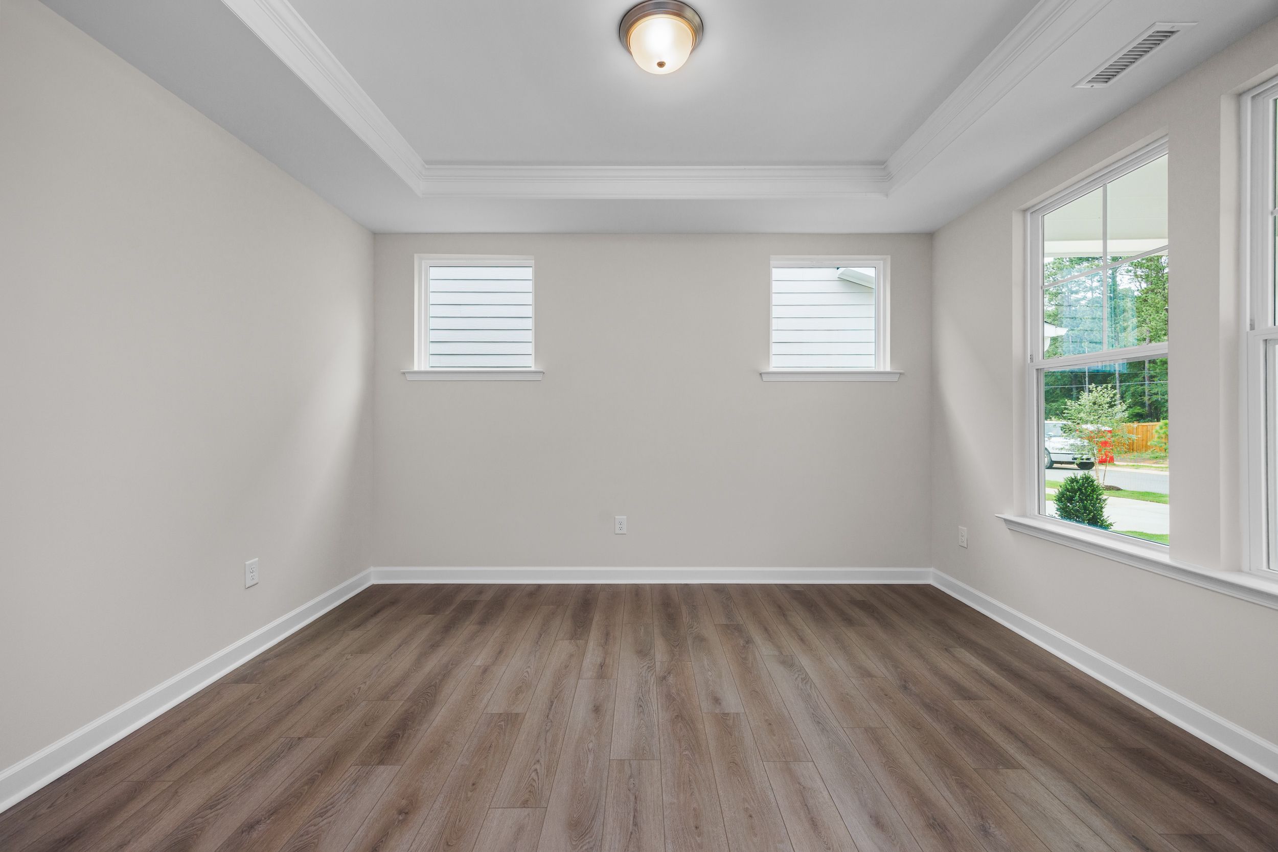Spacious master bedroom in The Aspen Davidson Homes with neutral walls, hardwood floors, tray ceiling, and large windows overlooking greenery