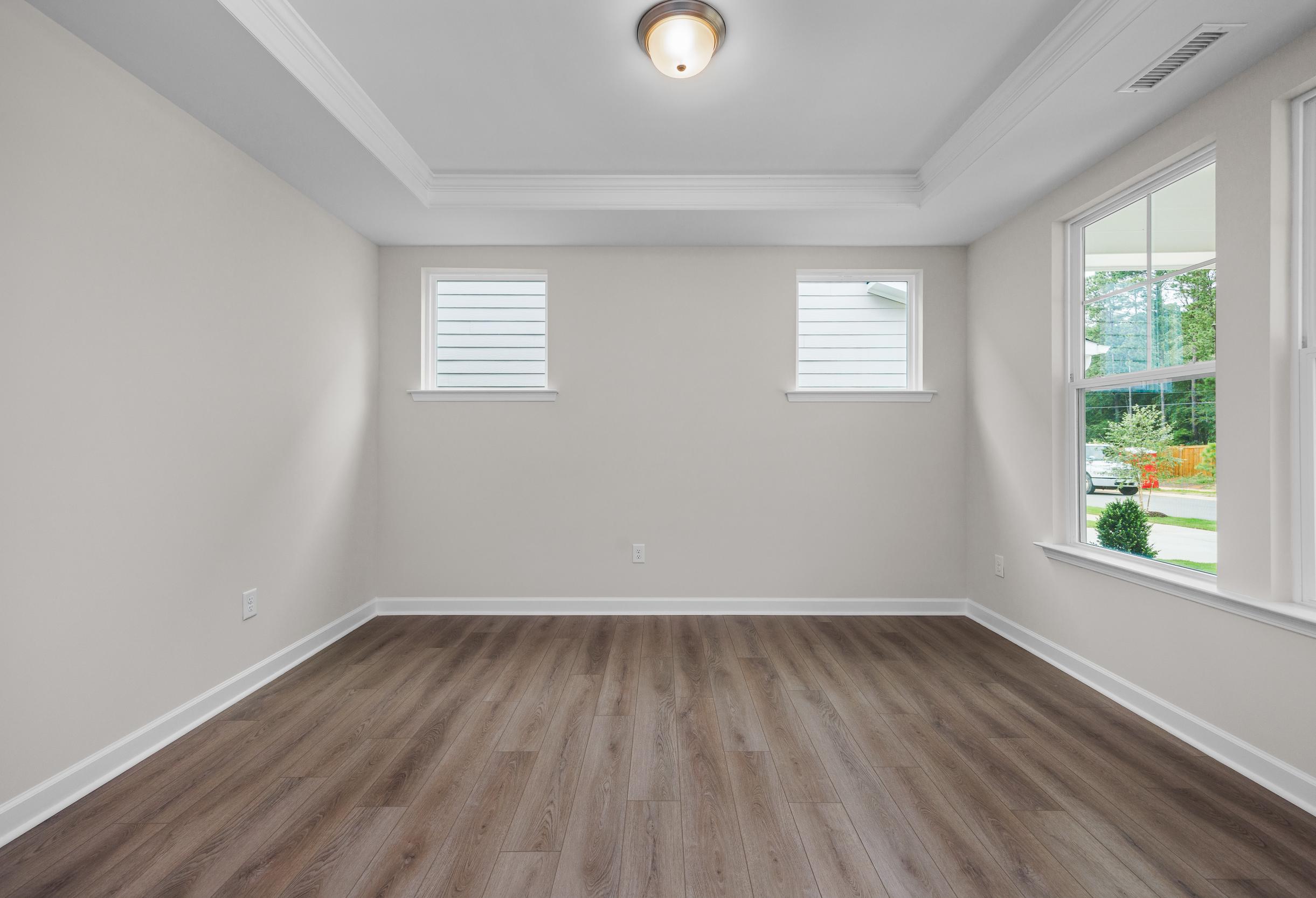 Spacious master bedroom in The Aspen Davidson Homes with neutral walls, hardwood floors, tray ceiling, and large windows overlooking greenery