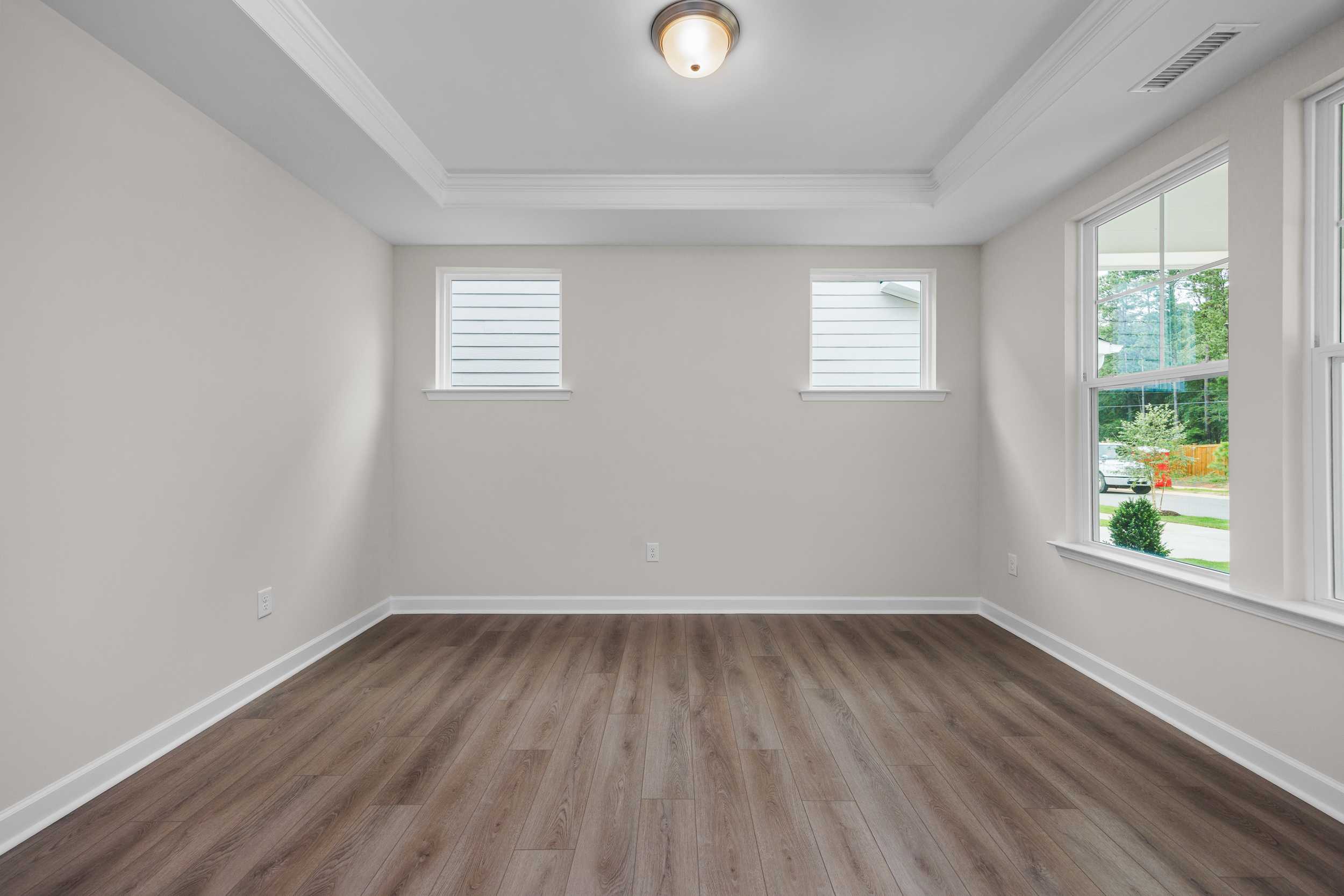 Spacious master bedroom in The Aspen Davidson Homes with neutral walls, hardwood floors, tray ceiling, and large windows overlooking greenery