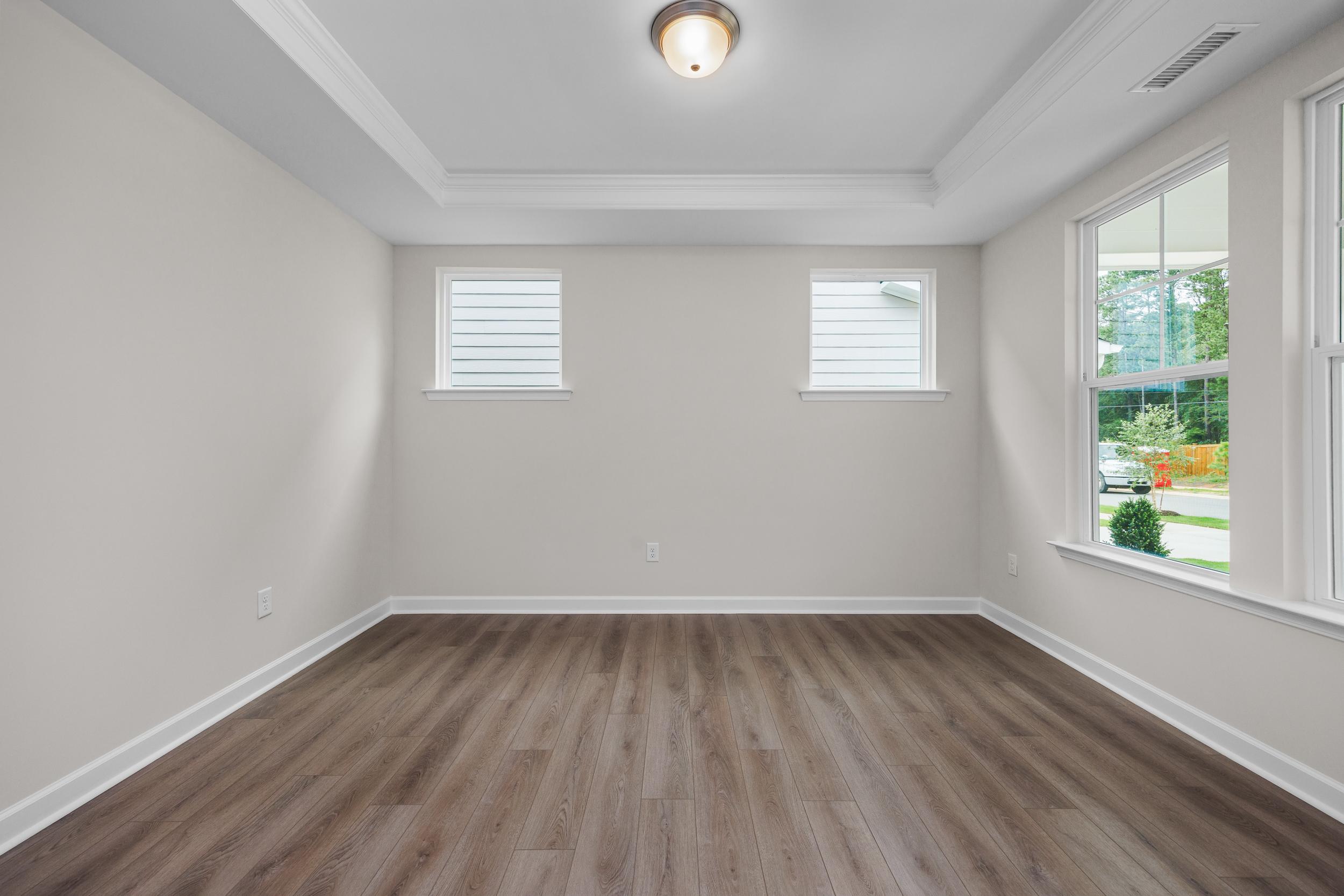 Spacious master bedroom in The Aspen Davidson Homes with neutral walls, hardwood floors, tray ceiling, and large windows overlooking greenery