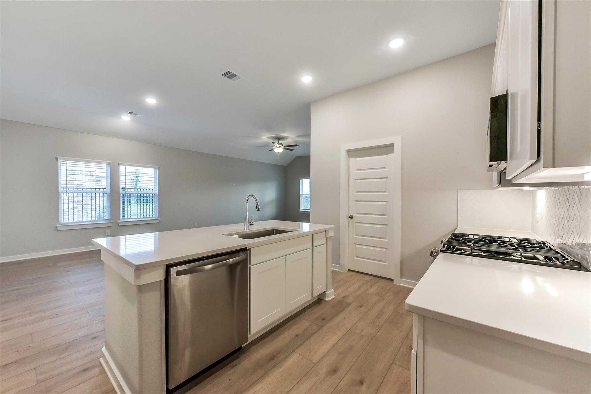 Modern open-concept kitchen with white quartz island, stainless dishwasher, gas range, and ceiling fan in Davidson Homes The Laguna B, Katy, Texas