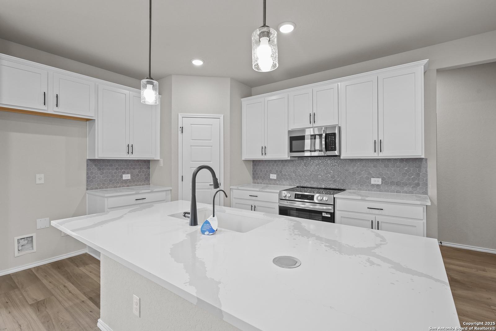 Modern white kitchen with quartz island sink, stainless steel appliances, and pendant lights in Davidson Homes The Murray J, San Antonio