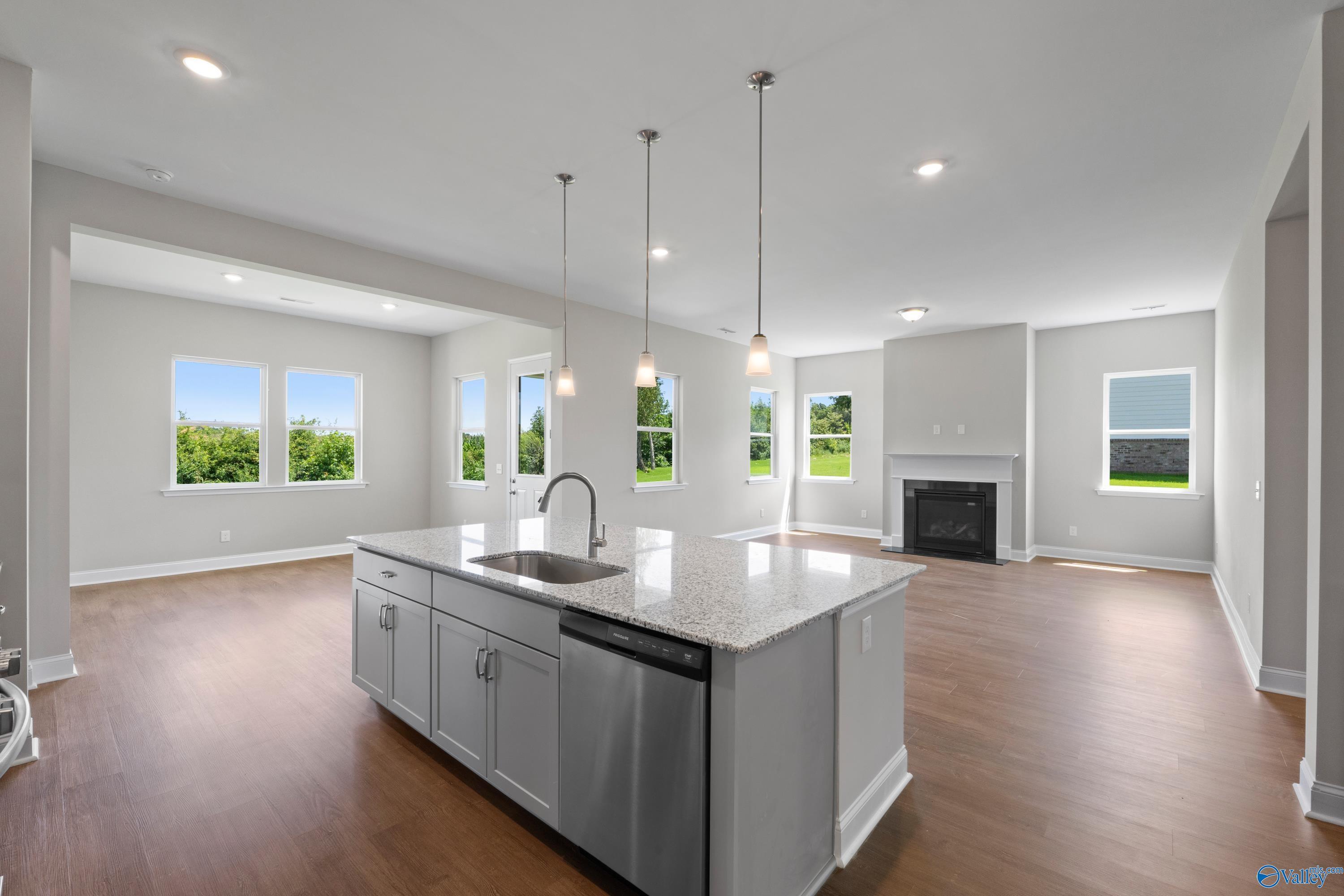 Modern open-concept kitchen with granite island, stainless dishwasher, pendant lights, and adjacent fireplace in The Arcadia home, Huntsville AL