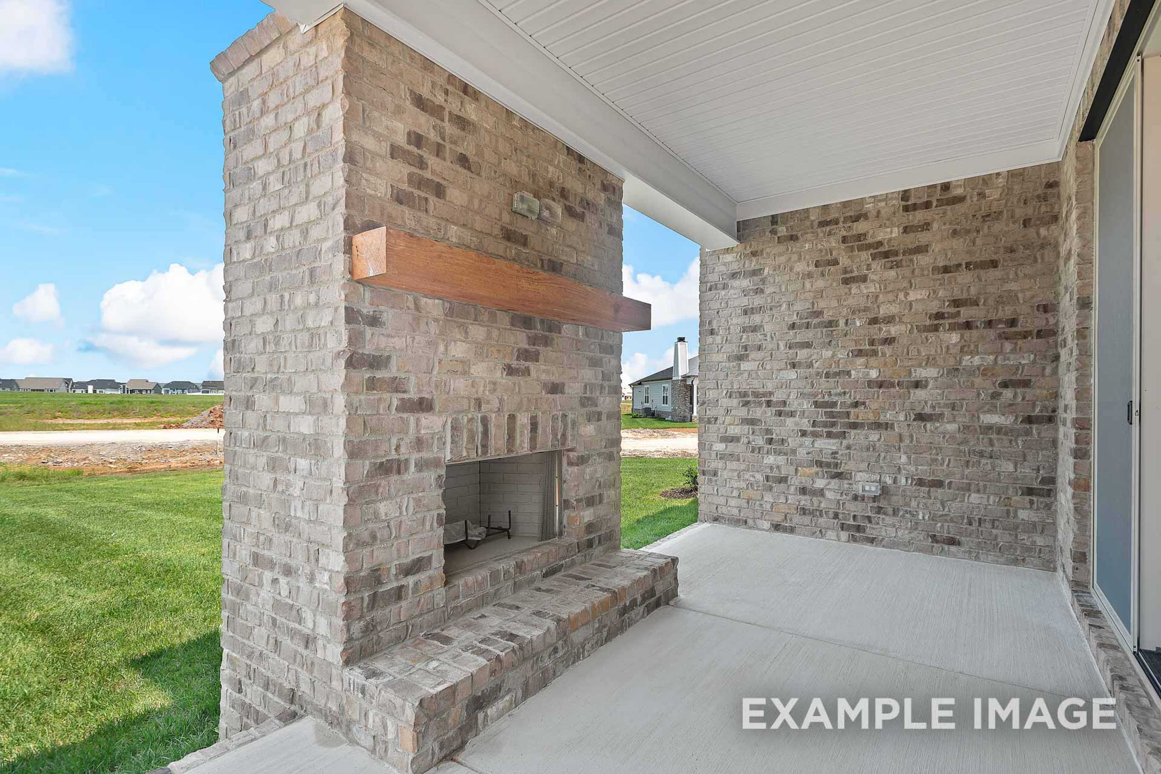 Spacious covered porch in The Hawkins with brick outdoor fireplace, wooden mantel, and lush green lawn