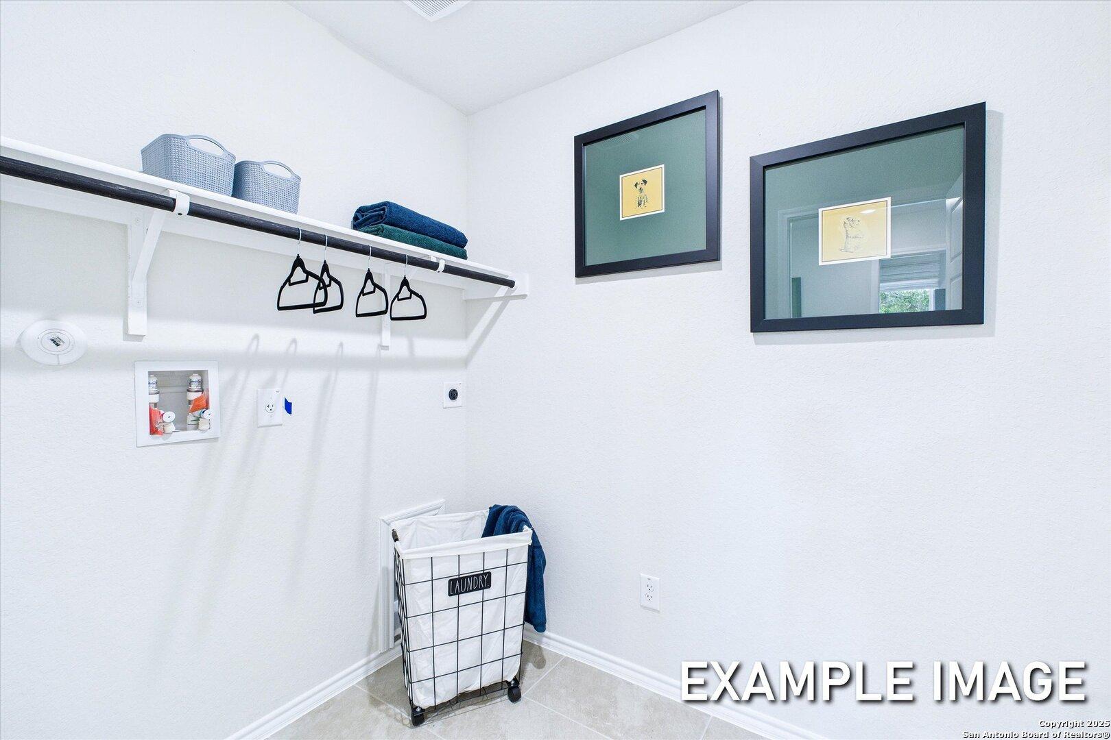 Bright laundry room with white shelving, garment rods, storage bins, and rolling hamper in Davidson Homes The Gillian C, San Antonio