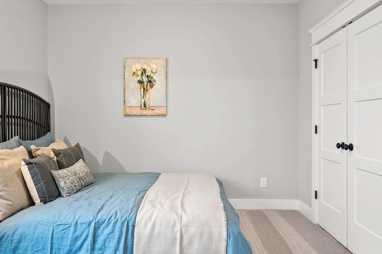 Spacious master bedroom in The Oxford featuring blue bedding, floral wall art, black headboard, and white closet doors