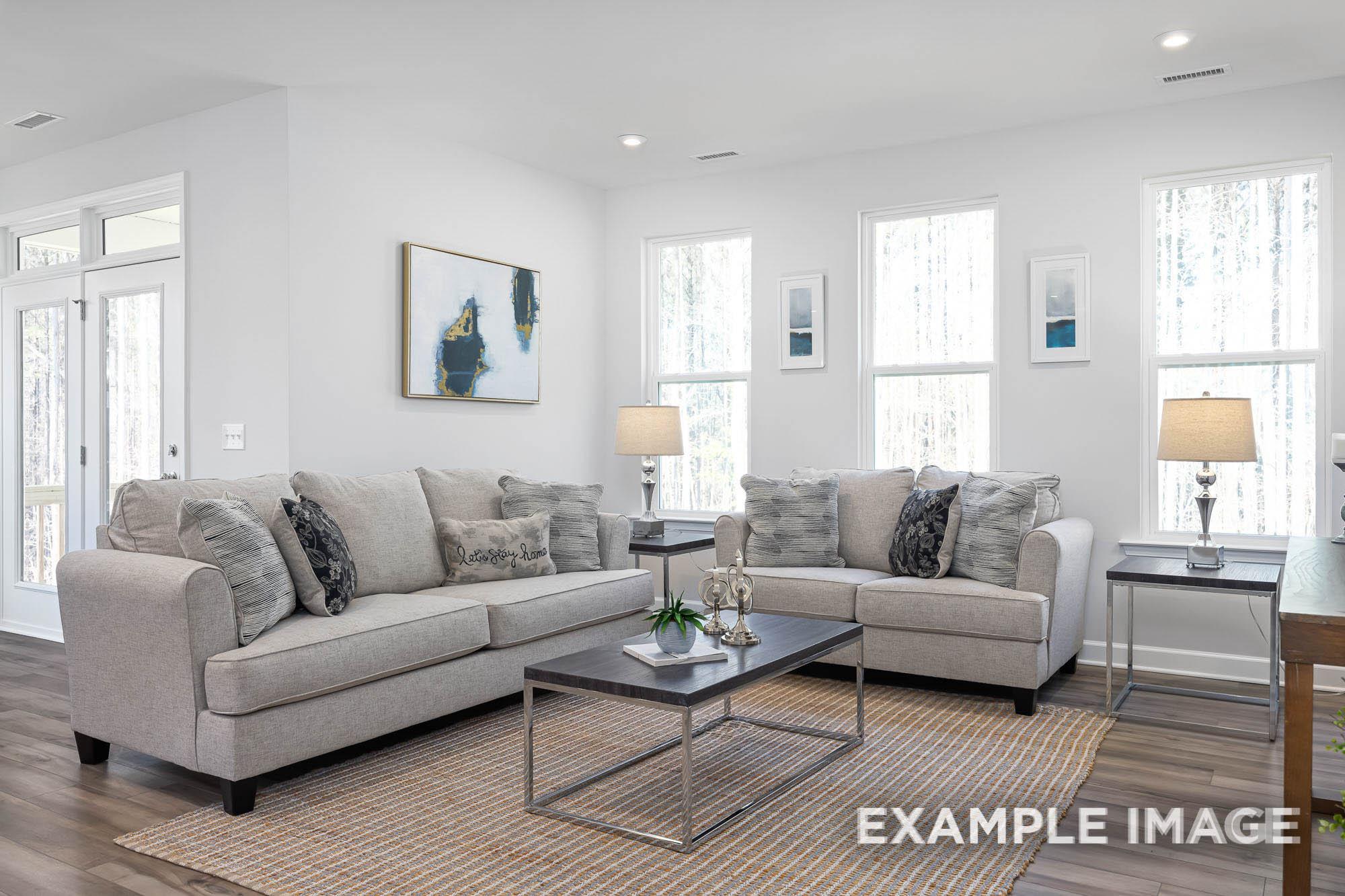 Spacious living room in The Ash home design featuring gray sectional sofas, modern coffee table, lamps, and large windows with natural light