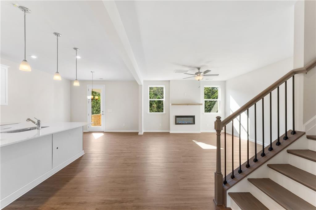 Open-concept kitchen and living room with white island, gas fireplace, hardwood floors, and staircase in Davidson Homes The Willow B, Dallas, Georgia