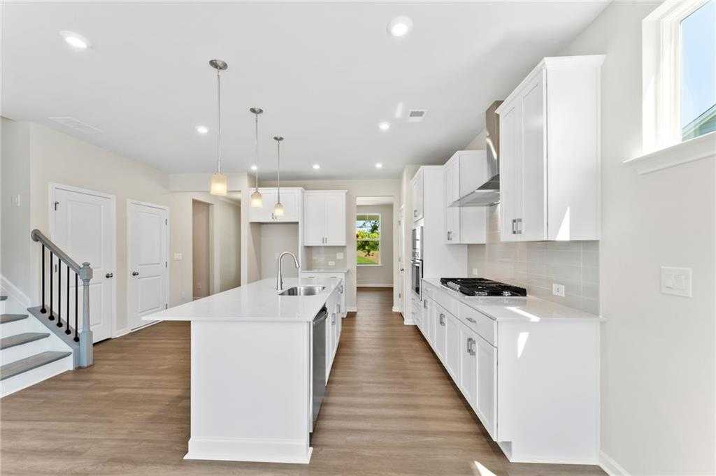 Modern white kitchen island with stainless appliances and hardwood floors in Davidson Homes The Ash B, Dallas, Georgia