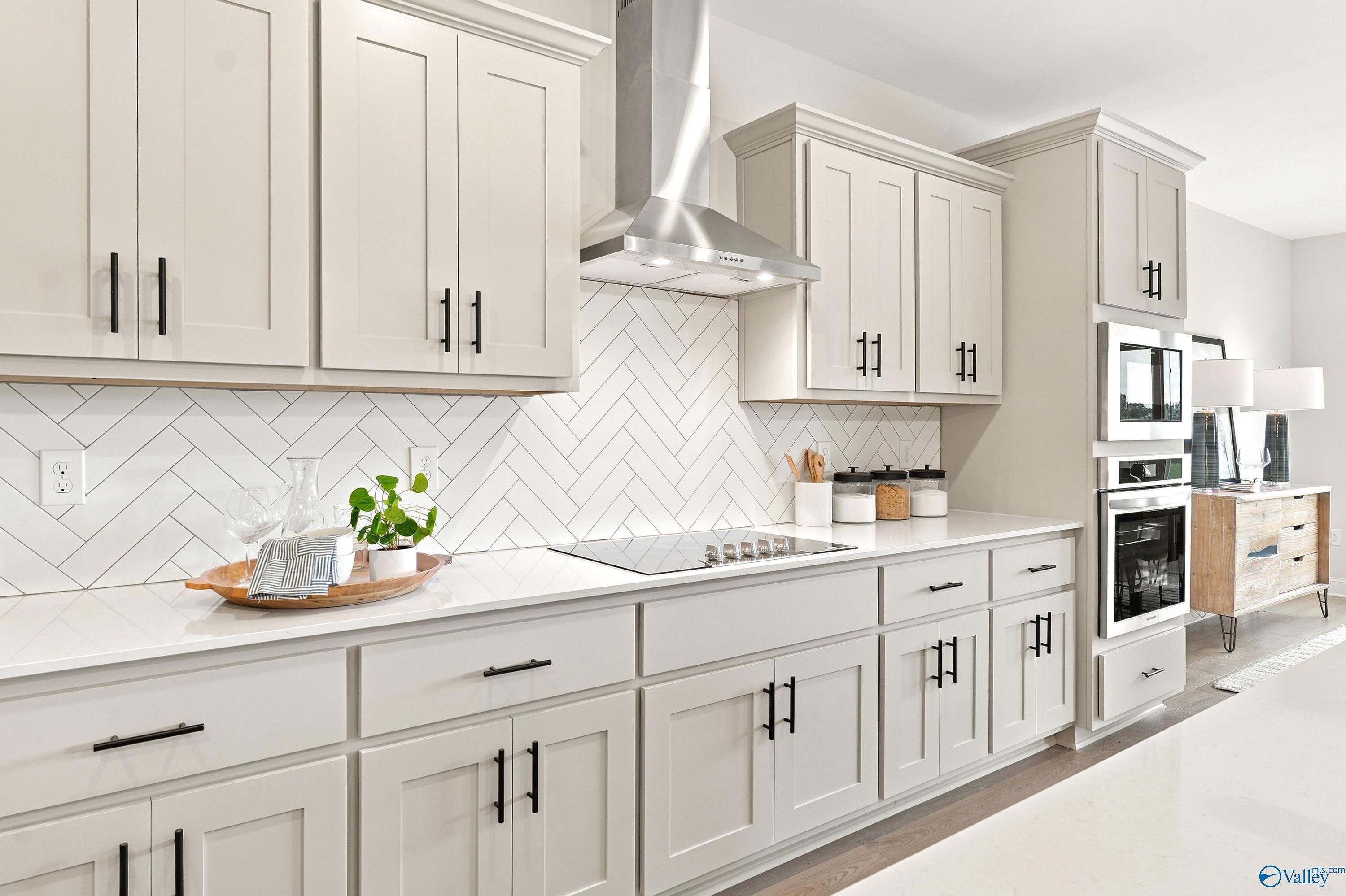 Modern kitchen with light gray cabinets, herringbone tile backsplash, and stainless appliances in The Finleigh, Huntsville.