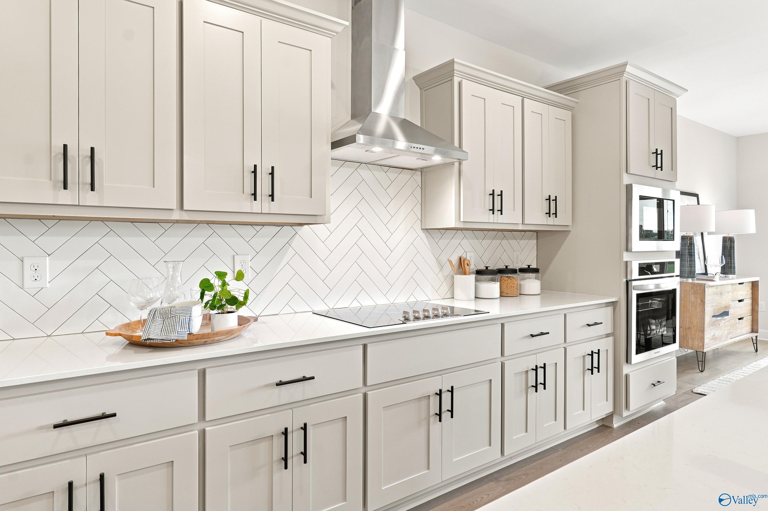 Modern kitchen with light gray cabinets, herringbone tile backsplash, and stainless appliances in The Finleigh, Huntsville.