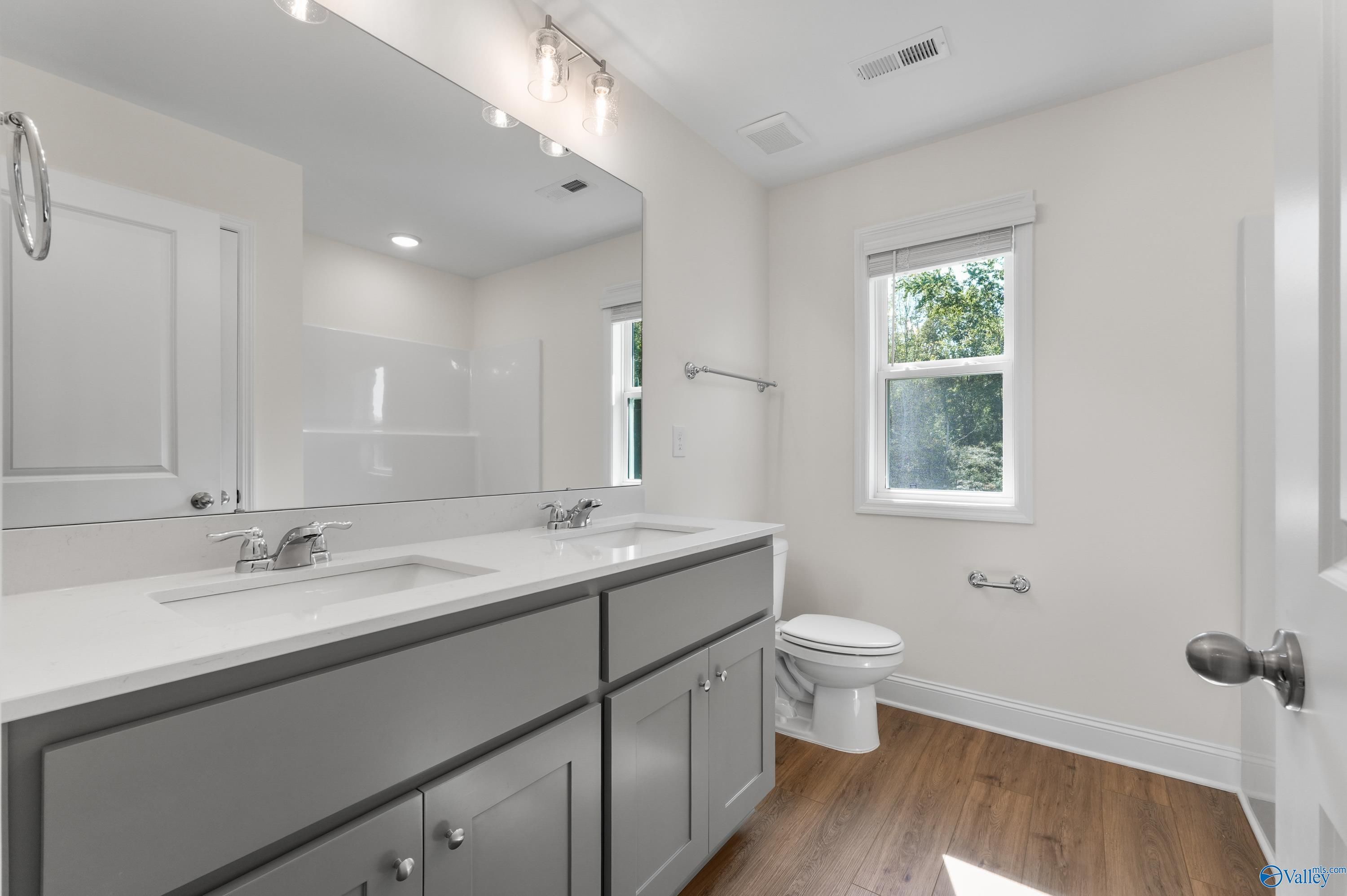 Modern bathroom with double vanity, gray cabinets, white quartz counters, and window in Davidson Homes The Shelby A, Athens AL
