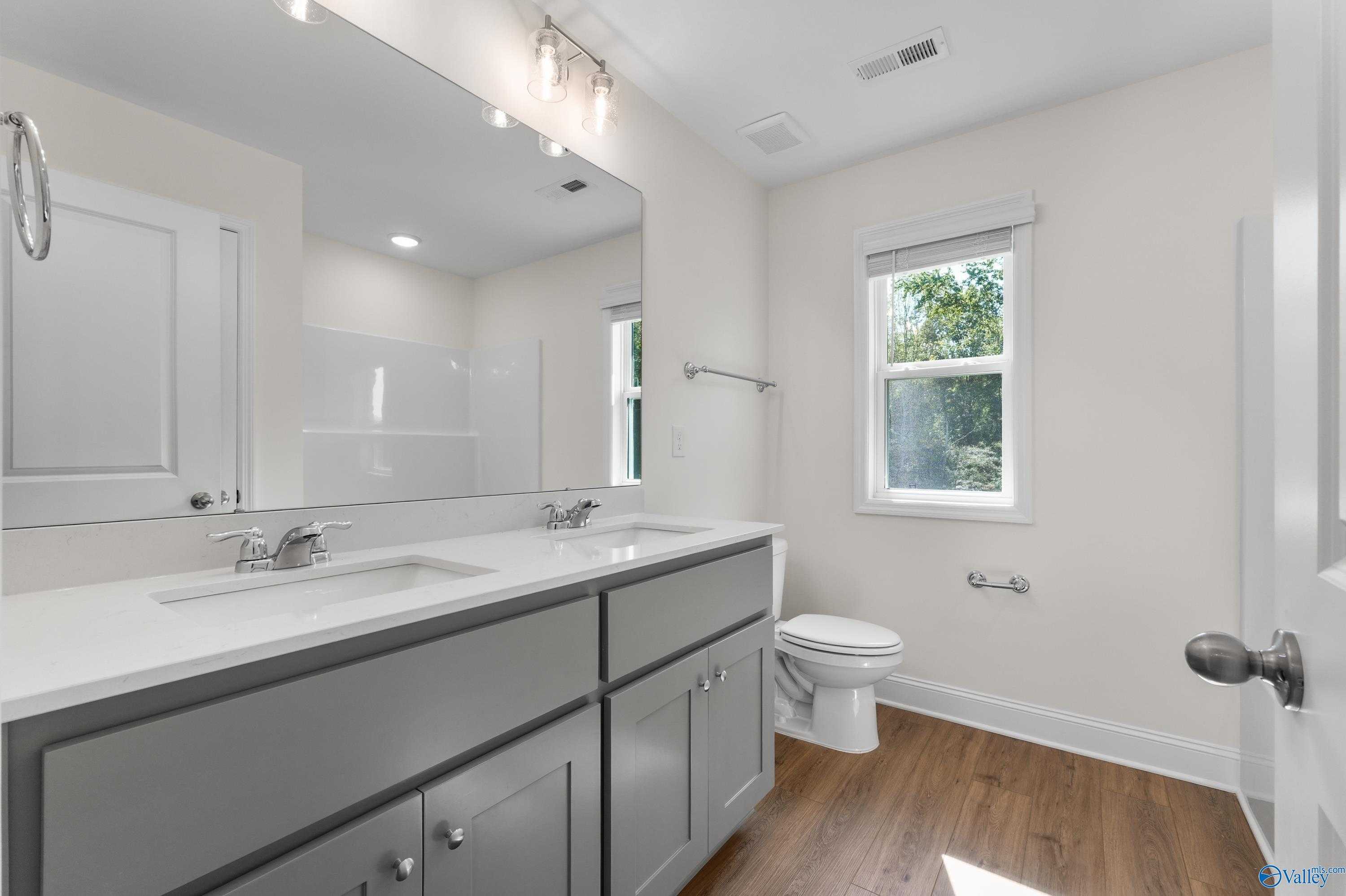 Bright bathroom with double sink vanity, gray cabinets, large mirror, and window in Davidson Homes The Shelby A, Athens, Alabama