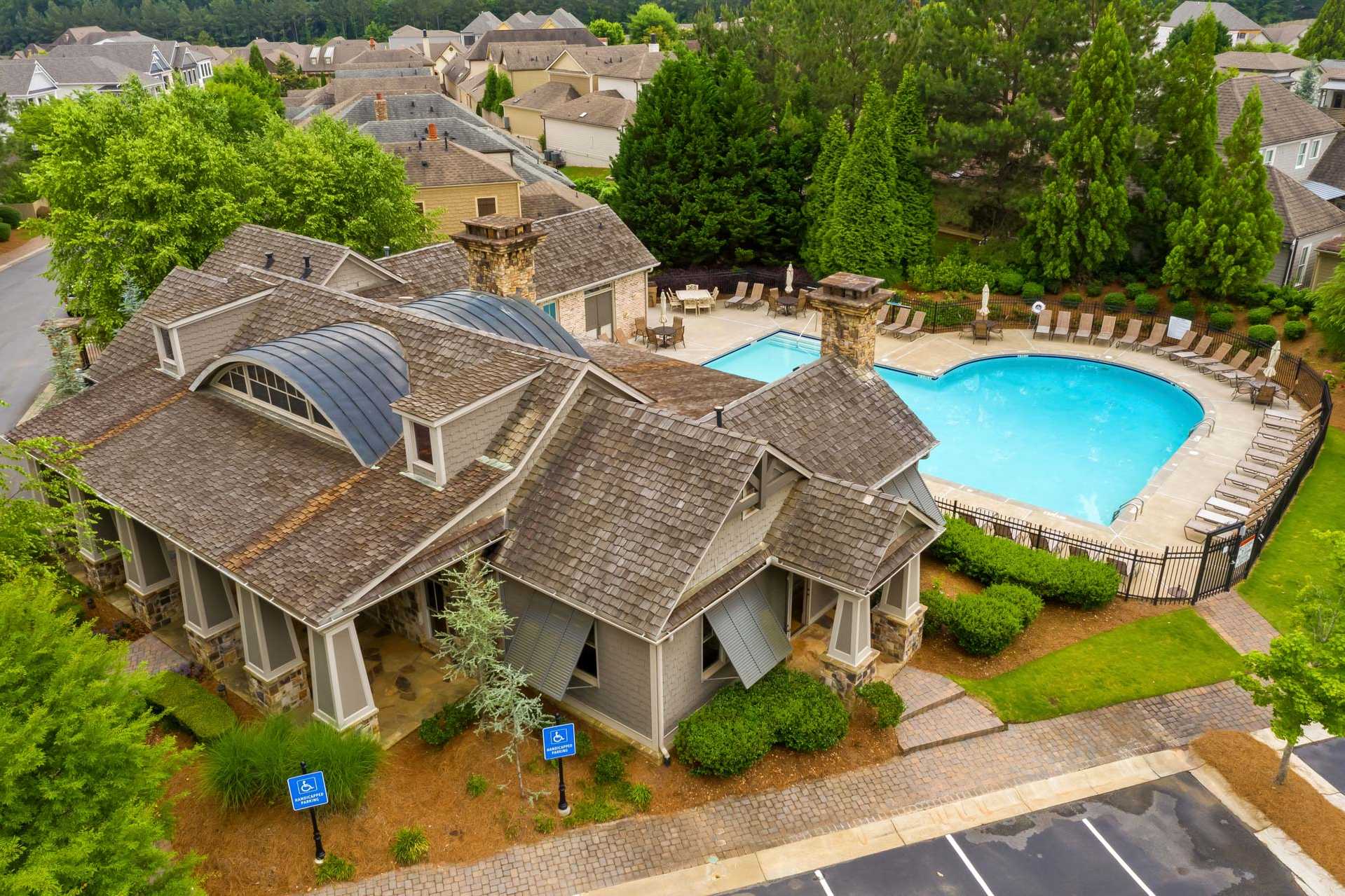 Clubhouse with shingled roof and heart-shaped swimming pool at The Village at Towne Lake in Woodstock GA featuring lounge chairs and lush landscaping