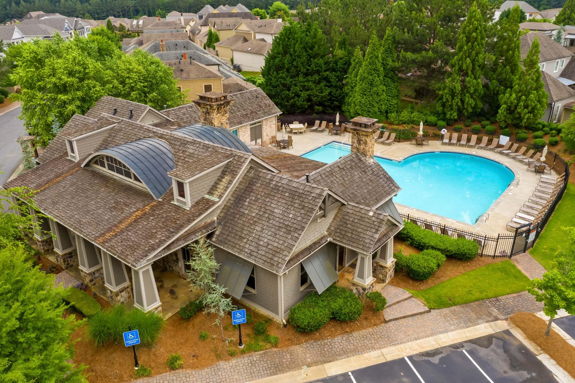 Clubhouse with shingled roof and heart-shaped swimming pool at The Village at Towne Lake in Woodstock GA featuring lounge chairs and lush landscaping