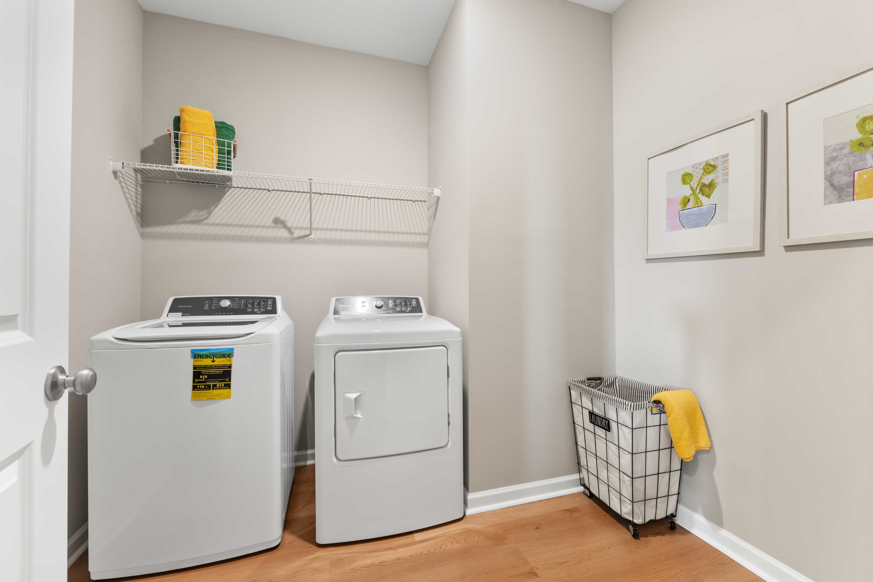 Spacious laundry room at The Meadows at Hampton Cove in Owens Cross Roads AL with white washer dryer, yellow towels, and hardwood floors
