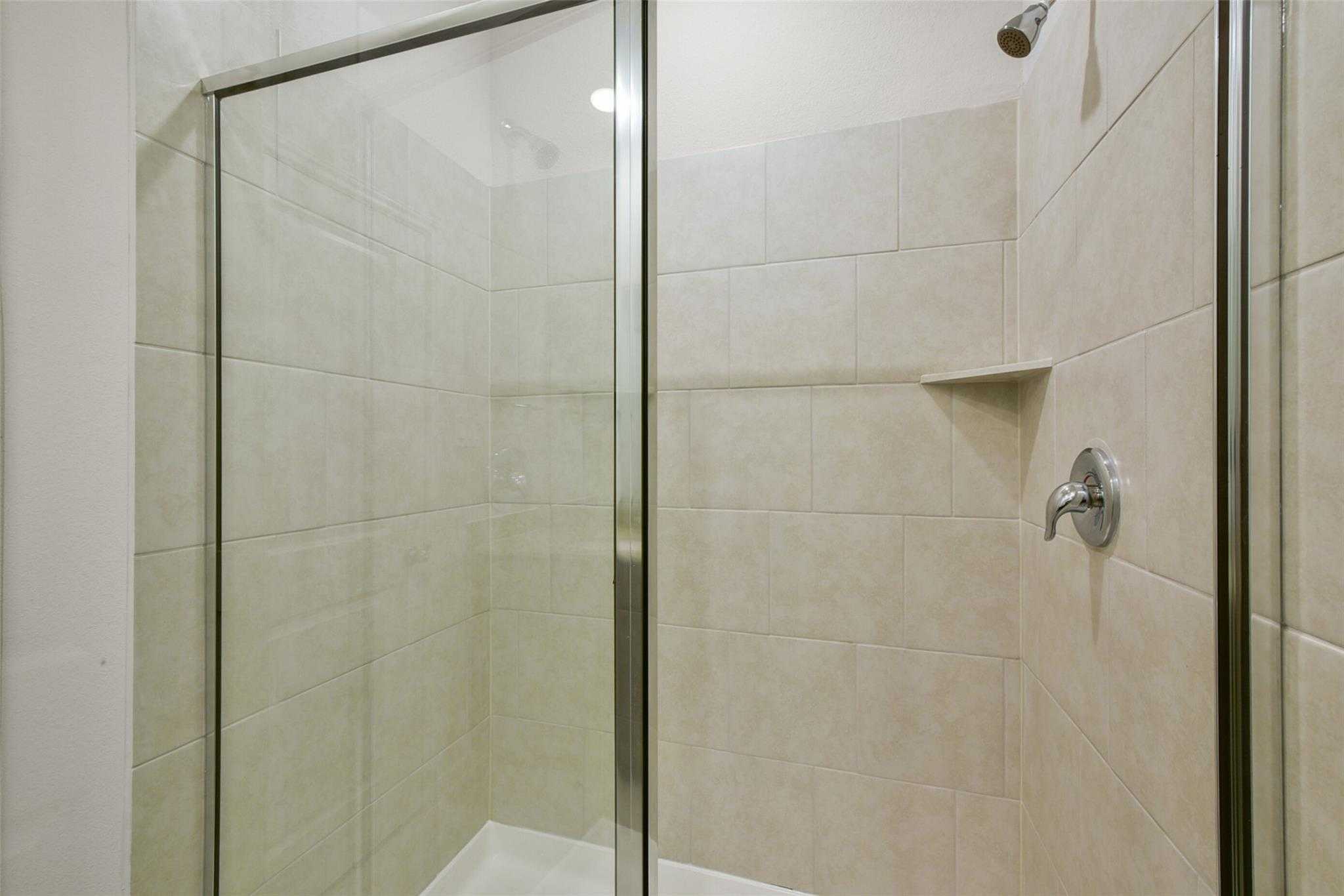 Modern glass shower enclosure with beige tiled walls and shelf in master bath of The Sabine E, Davidson Homes, Dayton, Texas