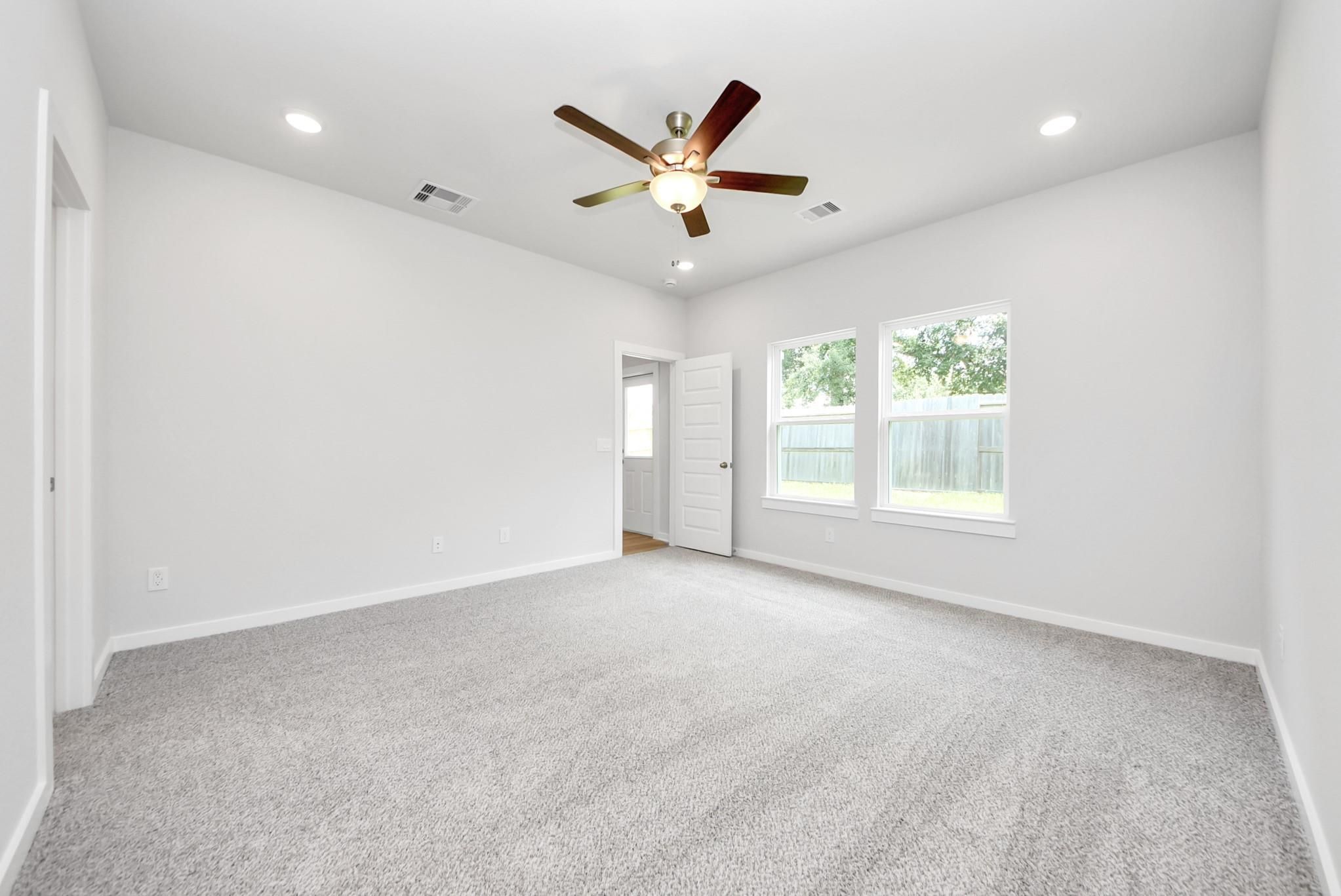 Spacious bedroom with grey carpet and ceiling fan in The Sabine E floor plan at Windmill Estates, Magnolia, Texas.