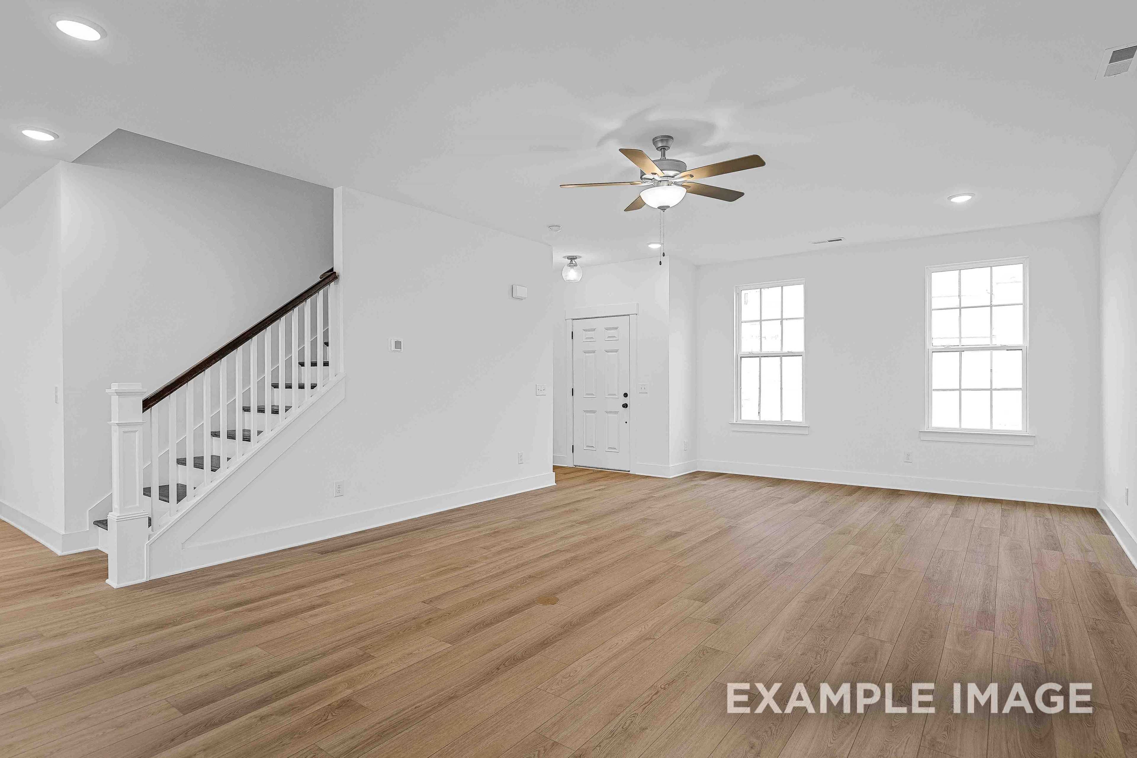 Spacious open-concept living area in The Charleston home plan featuring hardwood floors, white walls, large windows, and open staircase