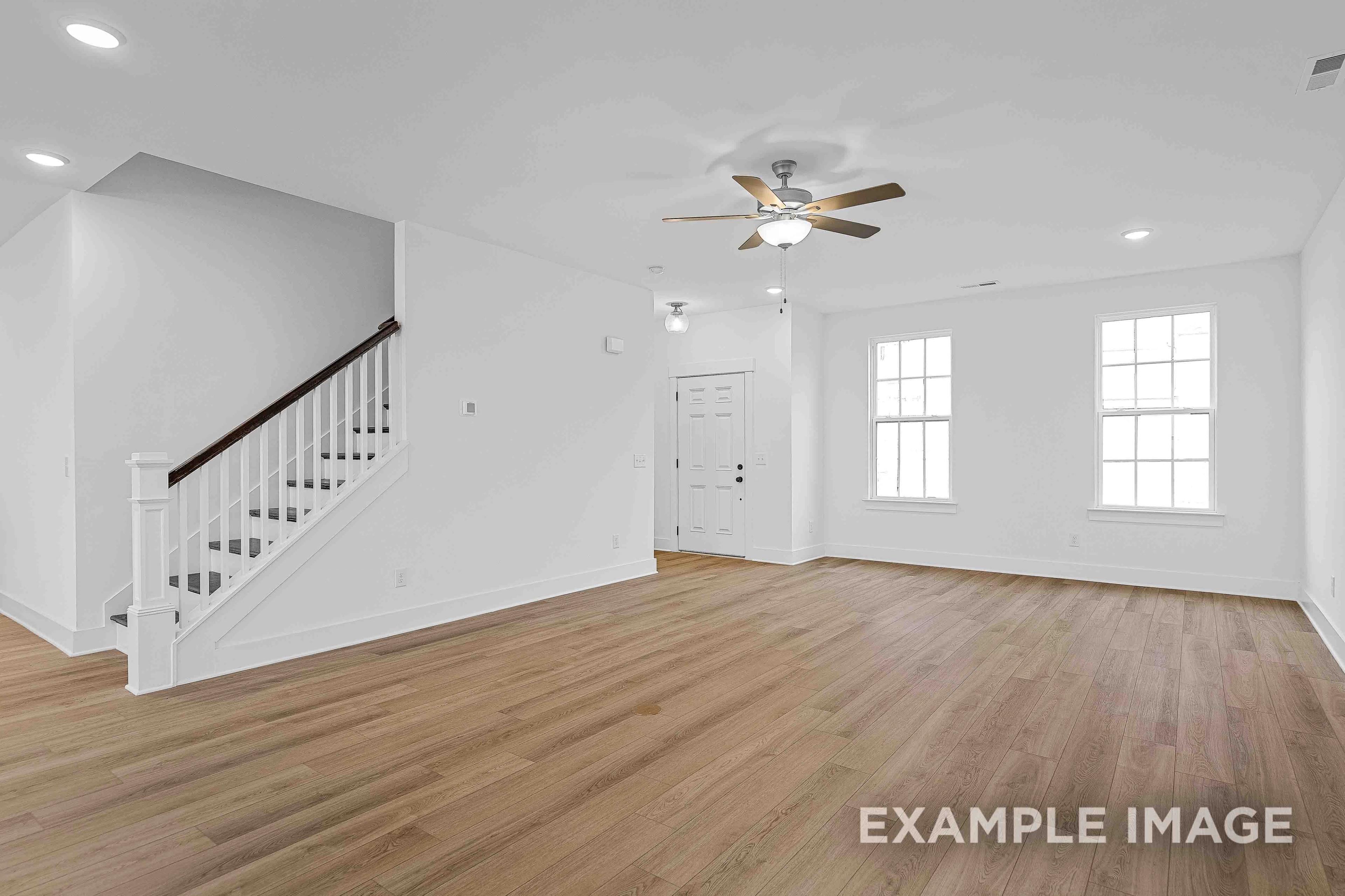 Spacious open-concept living area in The Charleston home plan featuring hardwood floors, white walls, large windows, and open staircase
