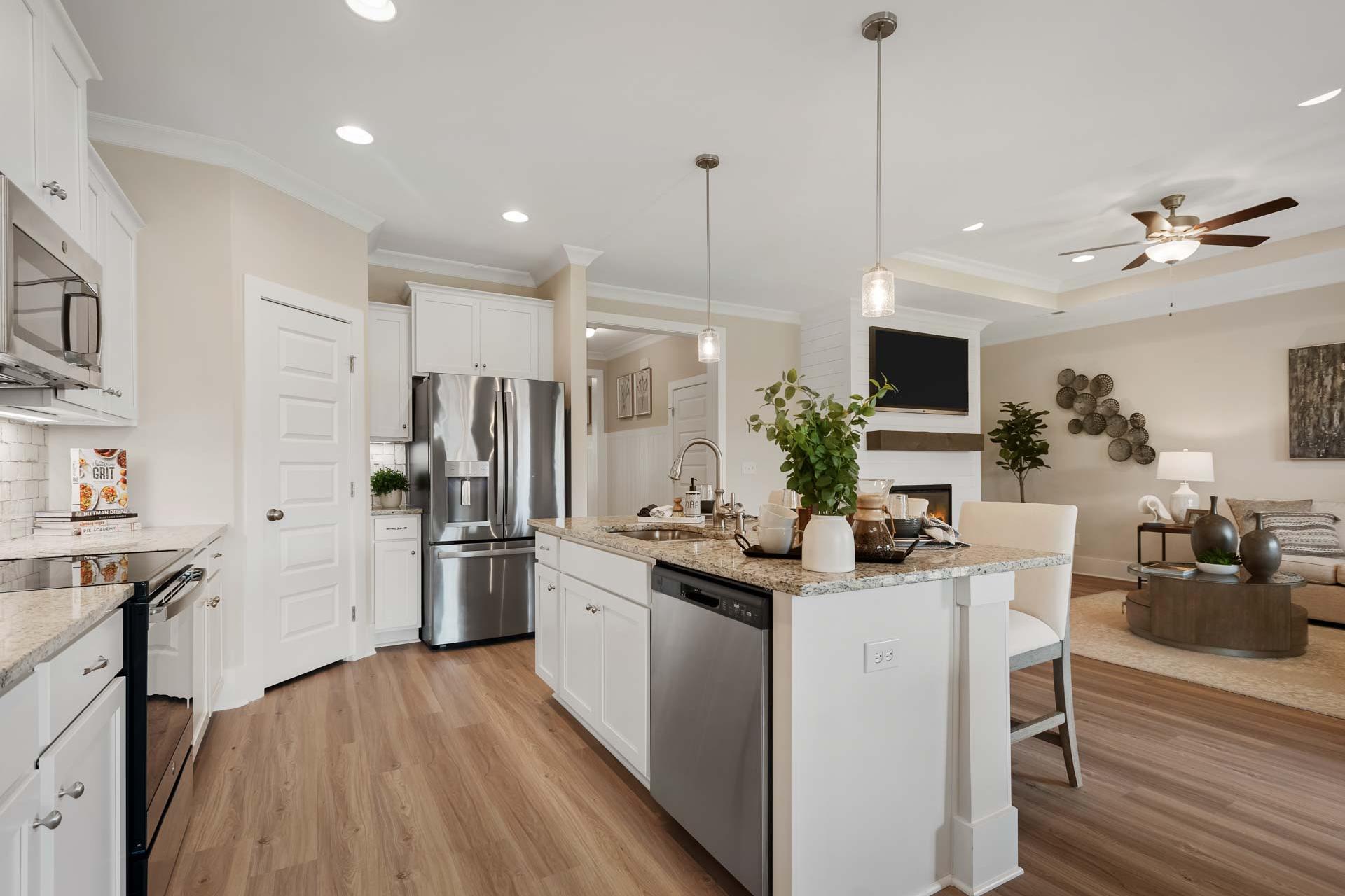 Open-concept kitchen and living room at Flint Meadows in New Market, Alabama featuring white cabinets, island bar and hardwood floors
