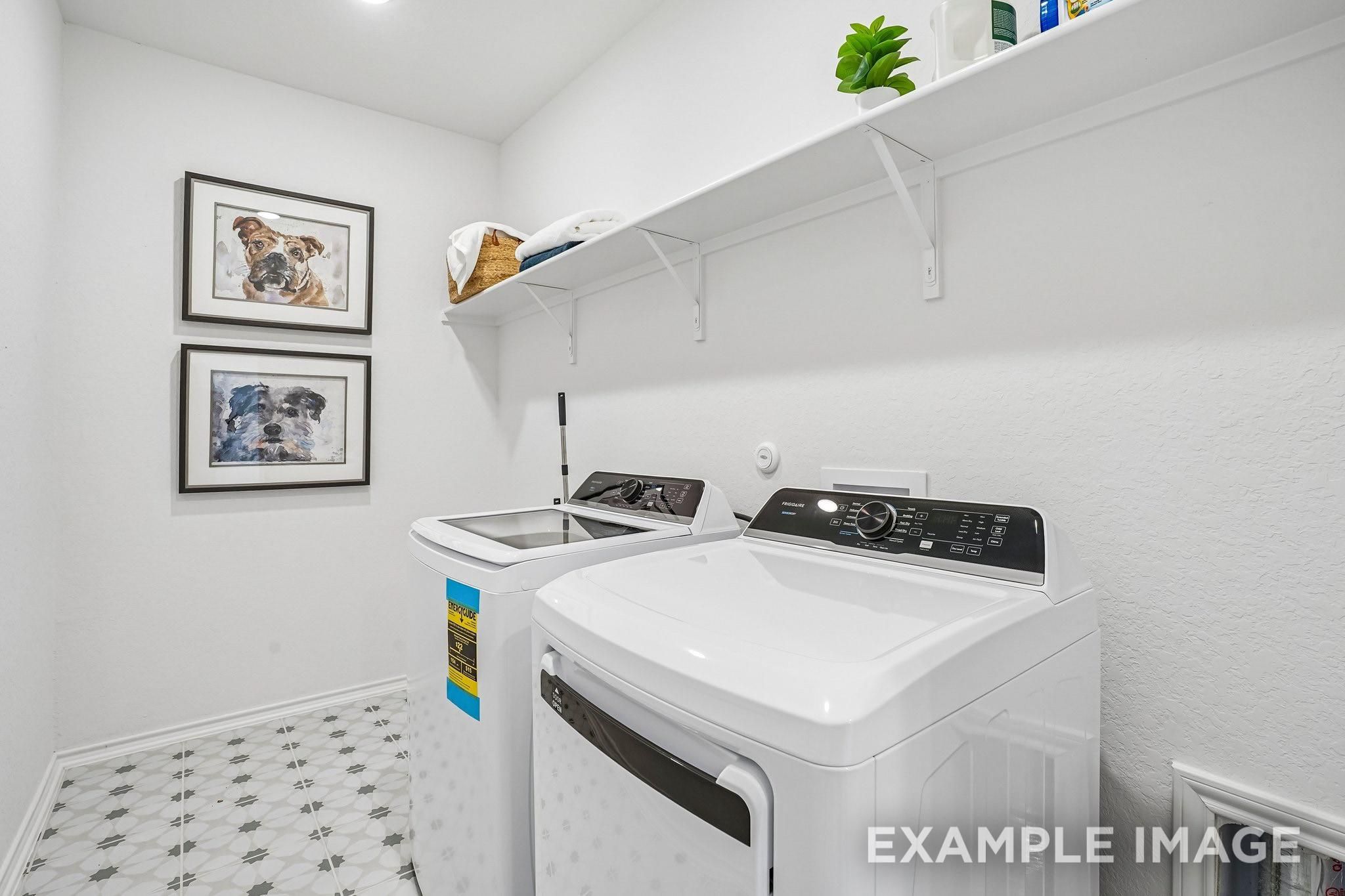 Bright laundry room with washer and dryer, white shelving, and patterned tile in Davidson Homes Ashport J, Crosby, Texas