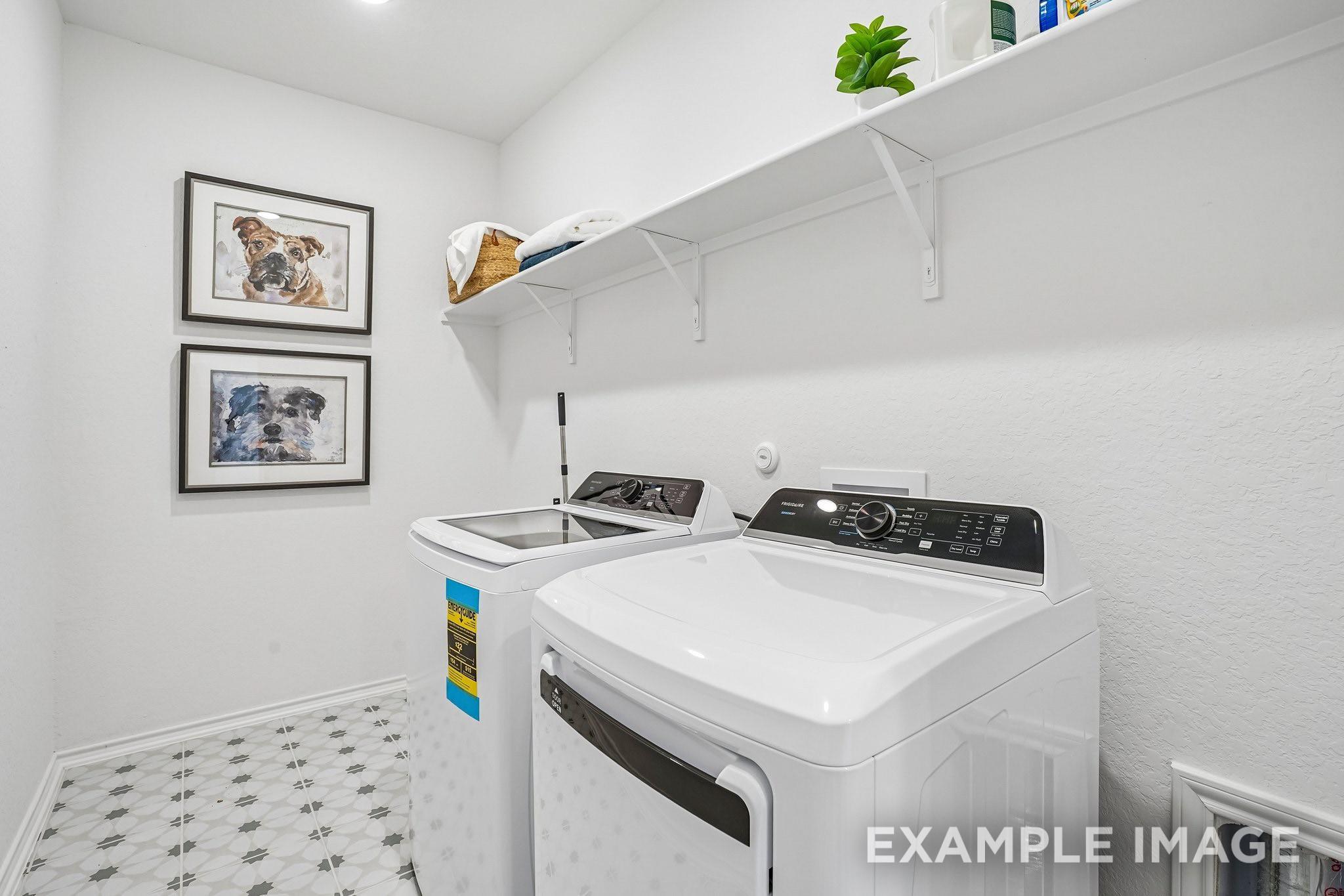 Bright laundry room with washer and dryer, white shelving, and patterned tile in Davidson Homes Ashport J, Crosby, Texas