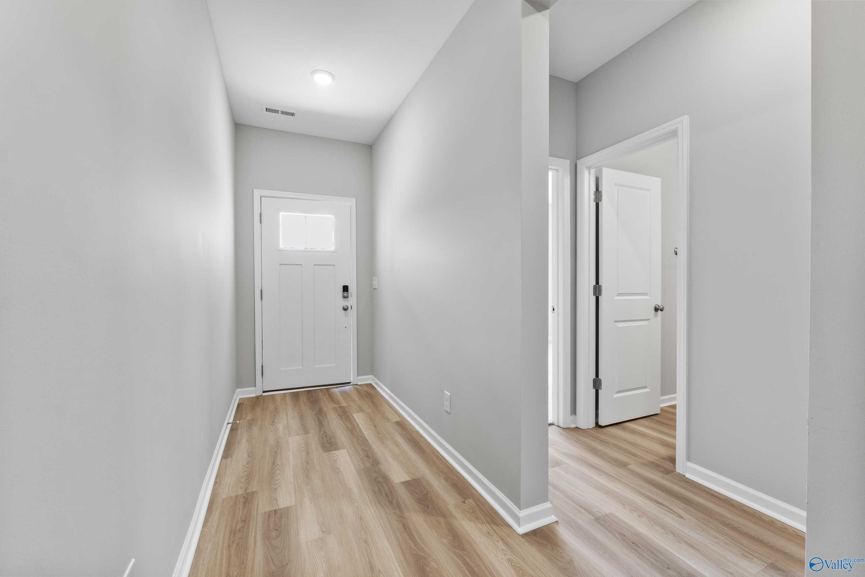 Bright hallway with light gray walls, white doors, and luxury vinyl plank flooring in The Phoenix 3-bedroom home, Hazel Green, Alabama