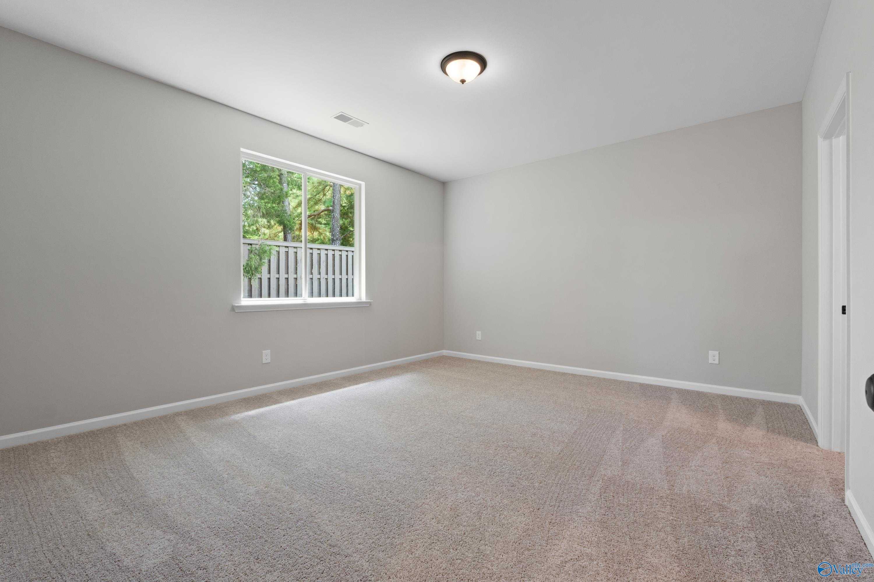 Bright secondary bedroom with light gray walls, beige carpet, and window overlooking greenery in The Nantucket home, Madison, Alabama